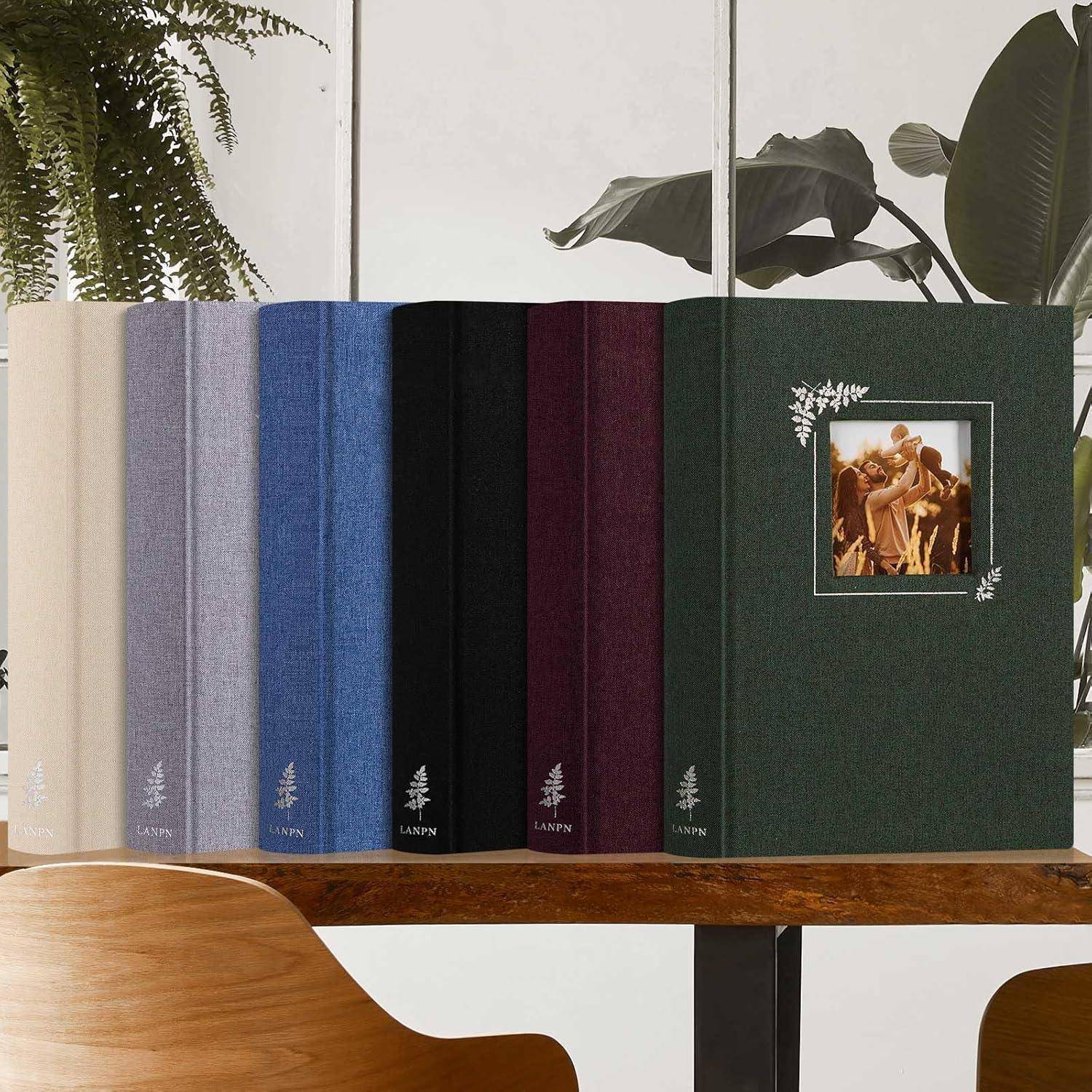 Eine Reihe von sechs Hardcover-Büchern in verschiedenen Farben, die auf einem Holztisch aufgereiht sind, wobei sich auf dem Einband des grünen Buches ein gerahmtes Bild befindet.