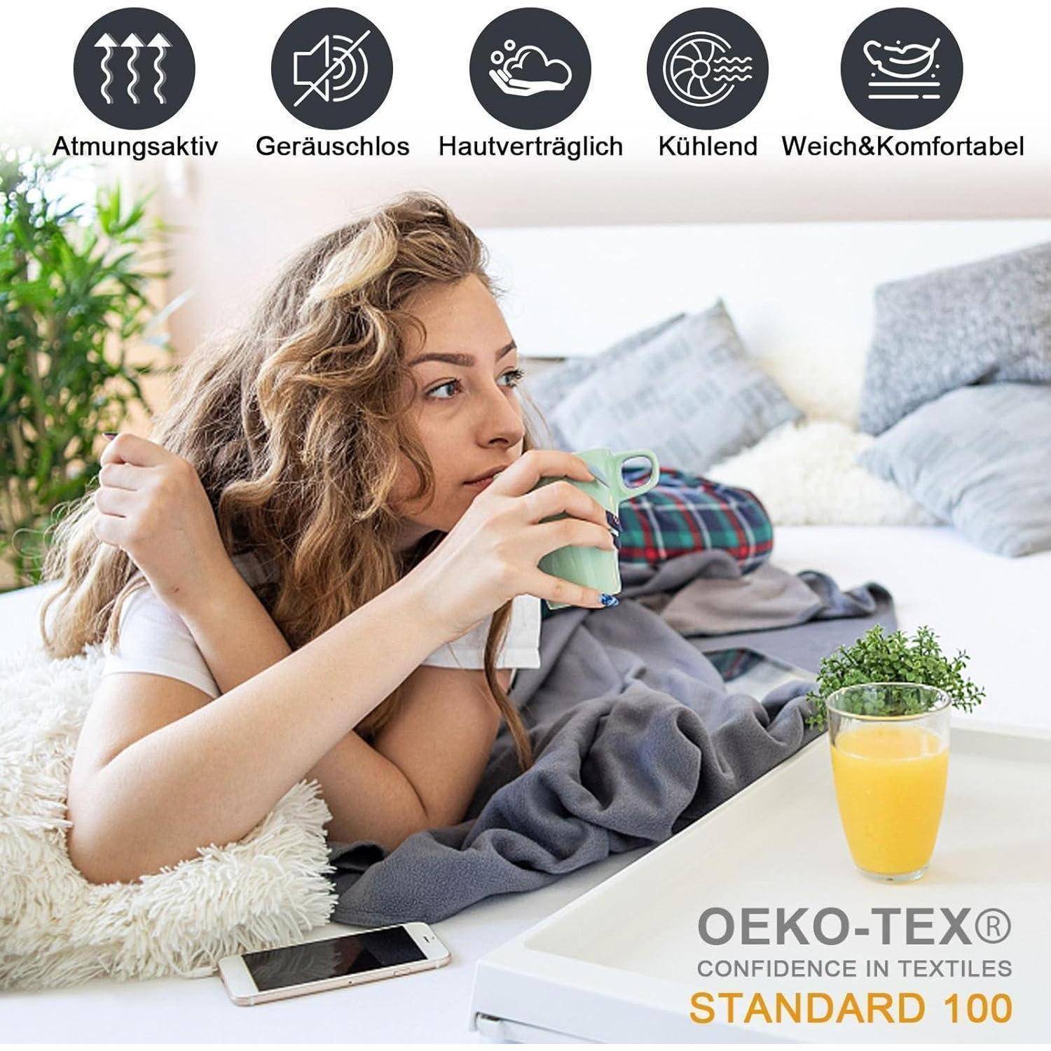Frau liegt auf dem Bett mit einem heißen Getränk, in eine graue Decke gehüllt. Icons über ihr stellen Stoff-Vorteile dar: atmungsaktiv, geräuscharm, hautfreundlich, kühlend, weich. OEKO-TEX Standard 100 Logo.