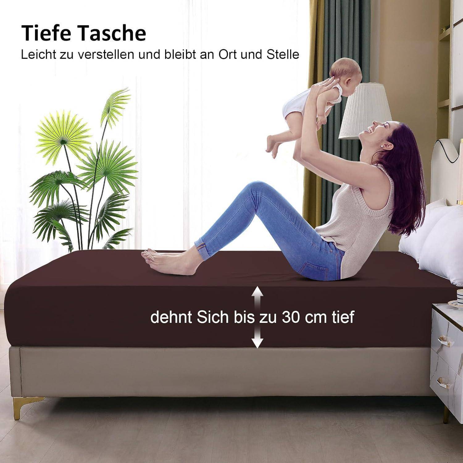 Eine Frau liegt auf einem Bett mit tiefen braunen Betttüchern und hebt ein Baby voller Freude. Text auf Deutsch beschreibt, dass sich das Bettlaken bis zu 30 cm dehnen lässt.