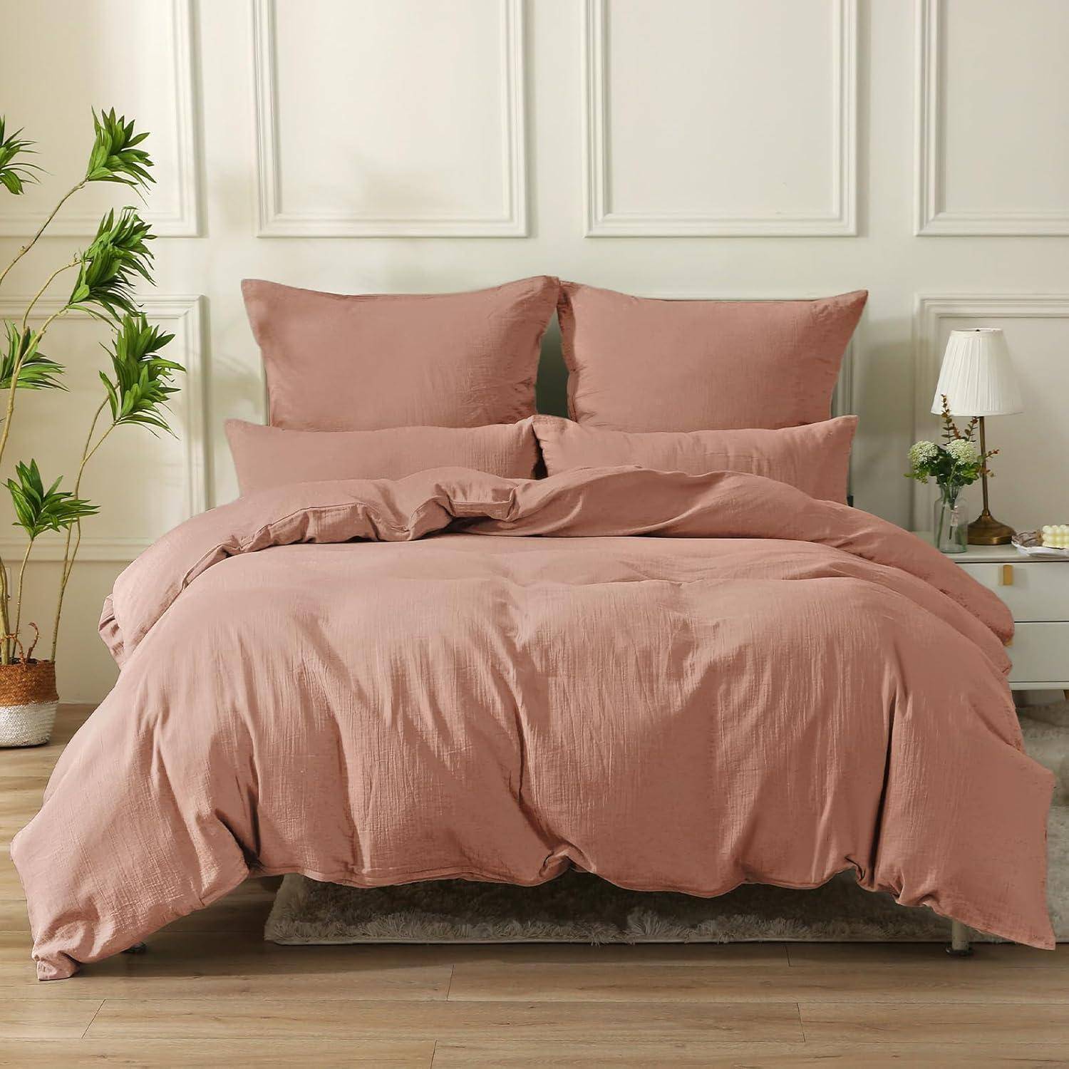 Ein ordentlich gemachtes Bett mit rosa Bettwäsche und zwei Kissen vor einer weißen Paneelwand. Ein kleiner Nachttisch mit einer Lampe und einer Pflanze ist zu sehen.