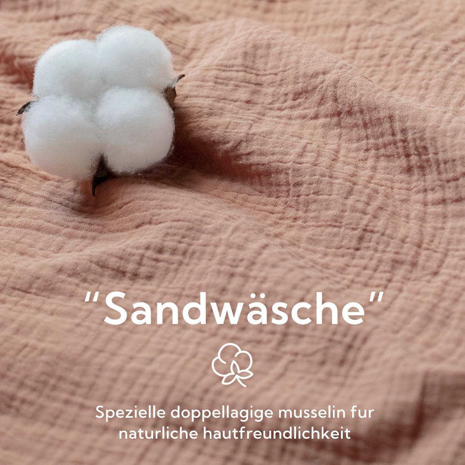 Eine flauschige Baumwollblüte auf einer strukturierten Stoffoberfläche; Text liest sich ‚Sandwäsche' und beschreibt es als ‚spezielle doppellagige musselin für natürliche hautfreundlichkeit'.