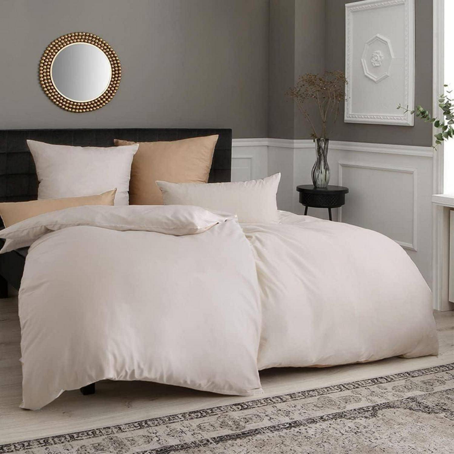 Ein gemütliches, elegant eingerichtetes Schlafzimmer mit einem großen Bett, weißer Bettwäsche, dekorativen Kissen, einem runden Spiegel und minimalistischer Einrichtung.