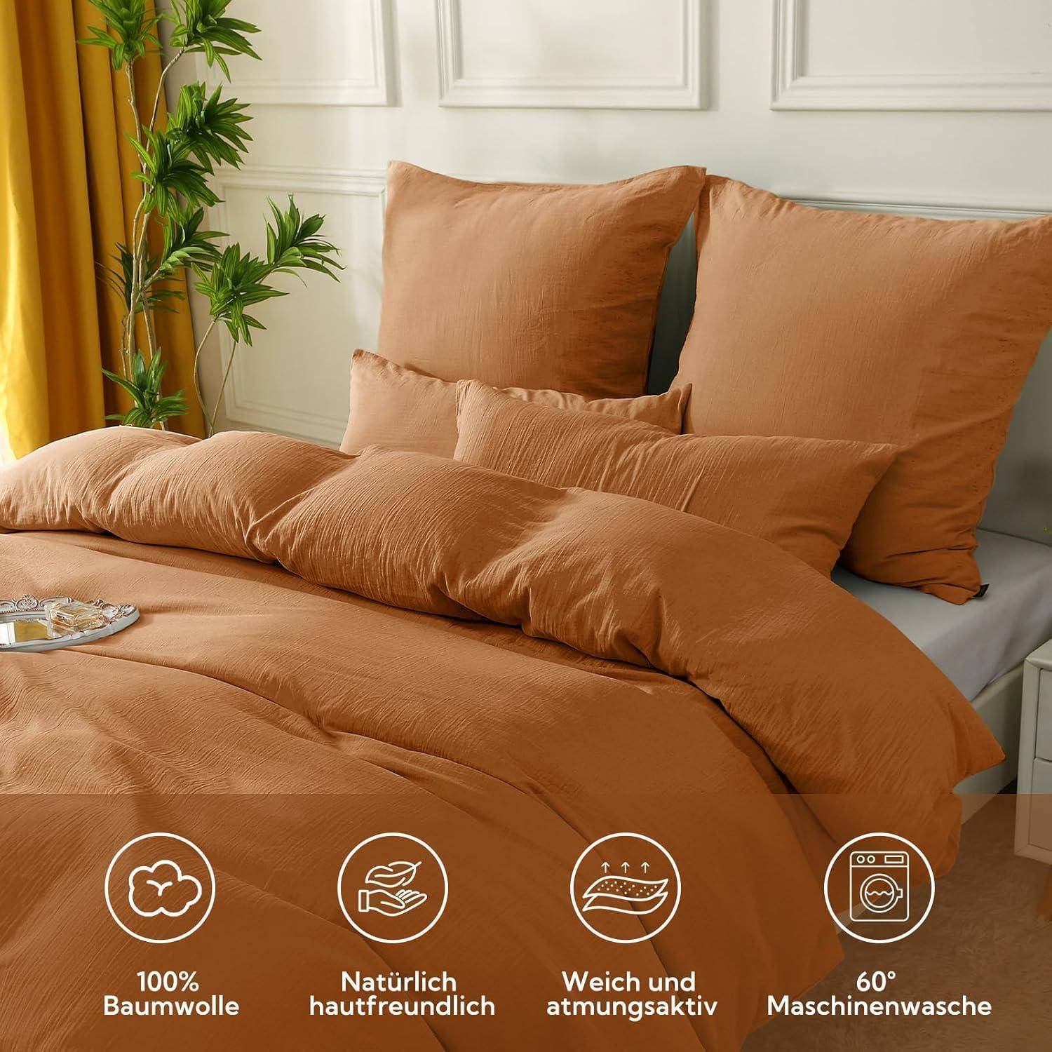 Schlafzimmerszene mit orangefarbener Bettwäsche, bestehend aus vier Kissen, einer Bettdecke, dekorativen Pflanzen und Symbolen, die das Baumwollmaterial und die Pflegeanweisungen hervorheben.