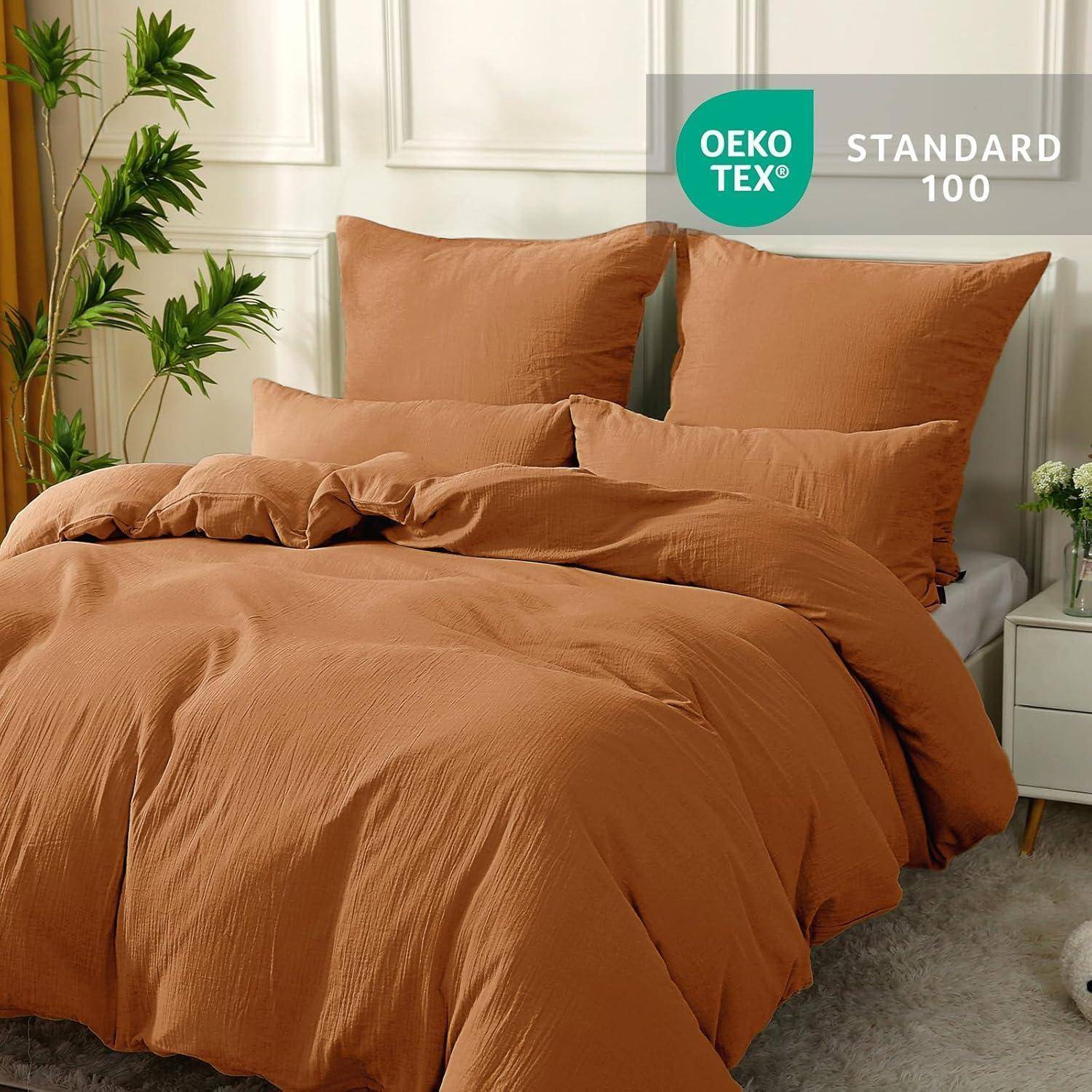 Rostfarbenes Bettwäsche-Set auf einem ordentlich gemachten Bett, mit dem Label 'Oeko-Tex Standard 100', daneben Pflanzen und ein Nachttisch.