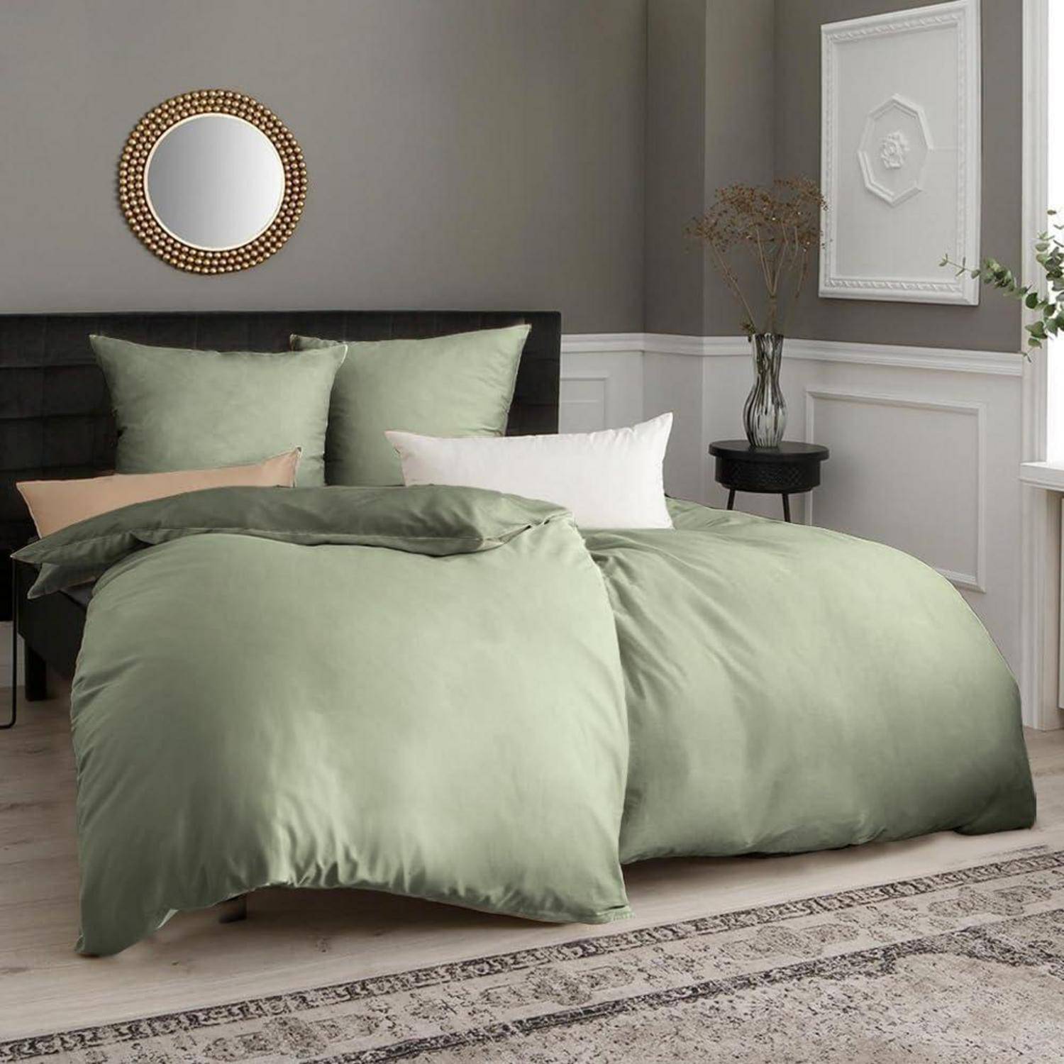 Ein gemütliches Schlafzimmer mit einem grünen Bettwäscheset, dekorativen Kissen, einem kleinen runden Spiegel und einem Beistelltisch mit einer hohen Pflanze.