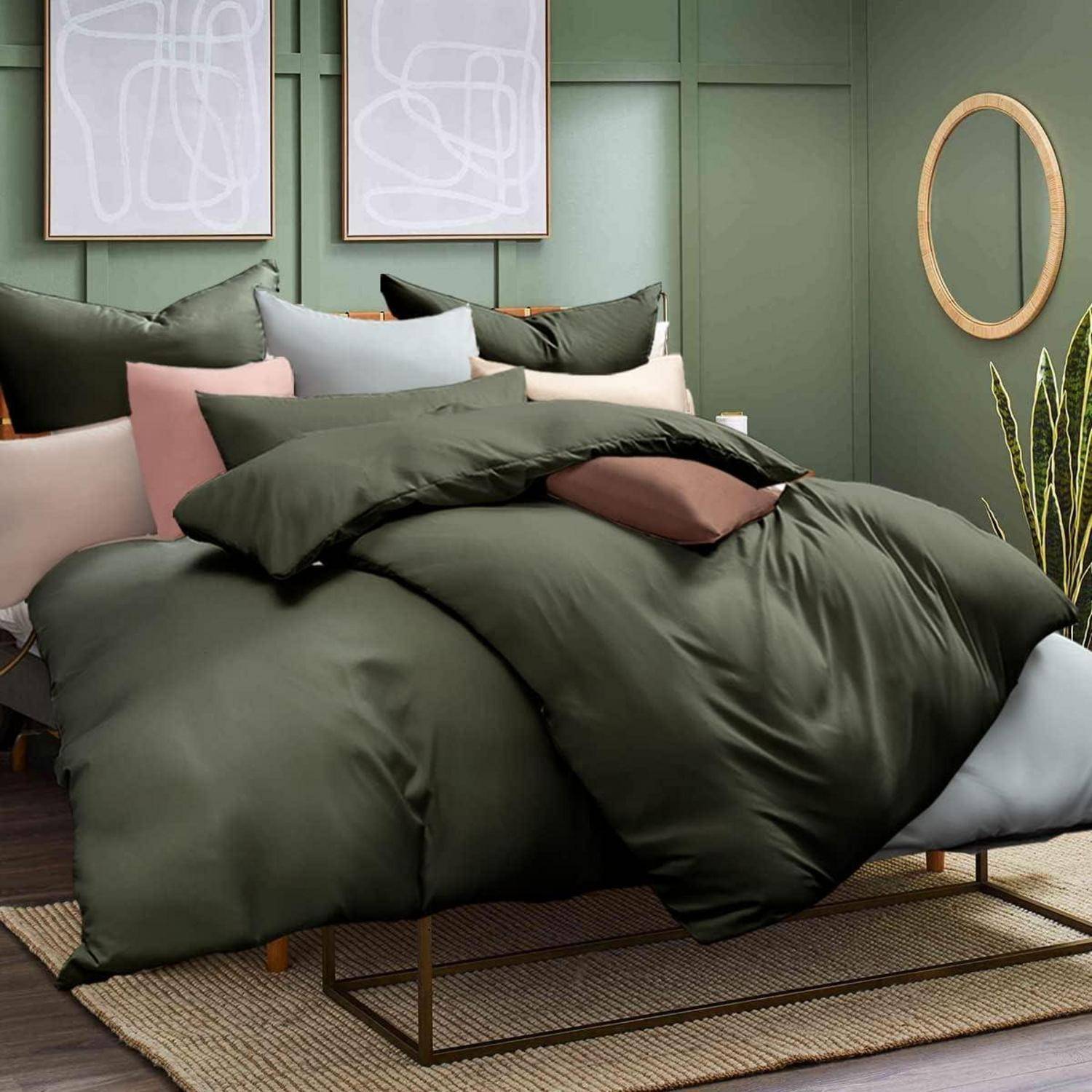 Ein sorgfältig gemachtes Bett mit dunkelgrüner Bettwäsche, mehreren Kissen und abstrakter Kunst an der Wand darüber. Moderne, gemütliche Schlafzimmereinrichtung.
