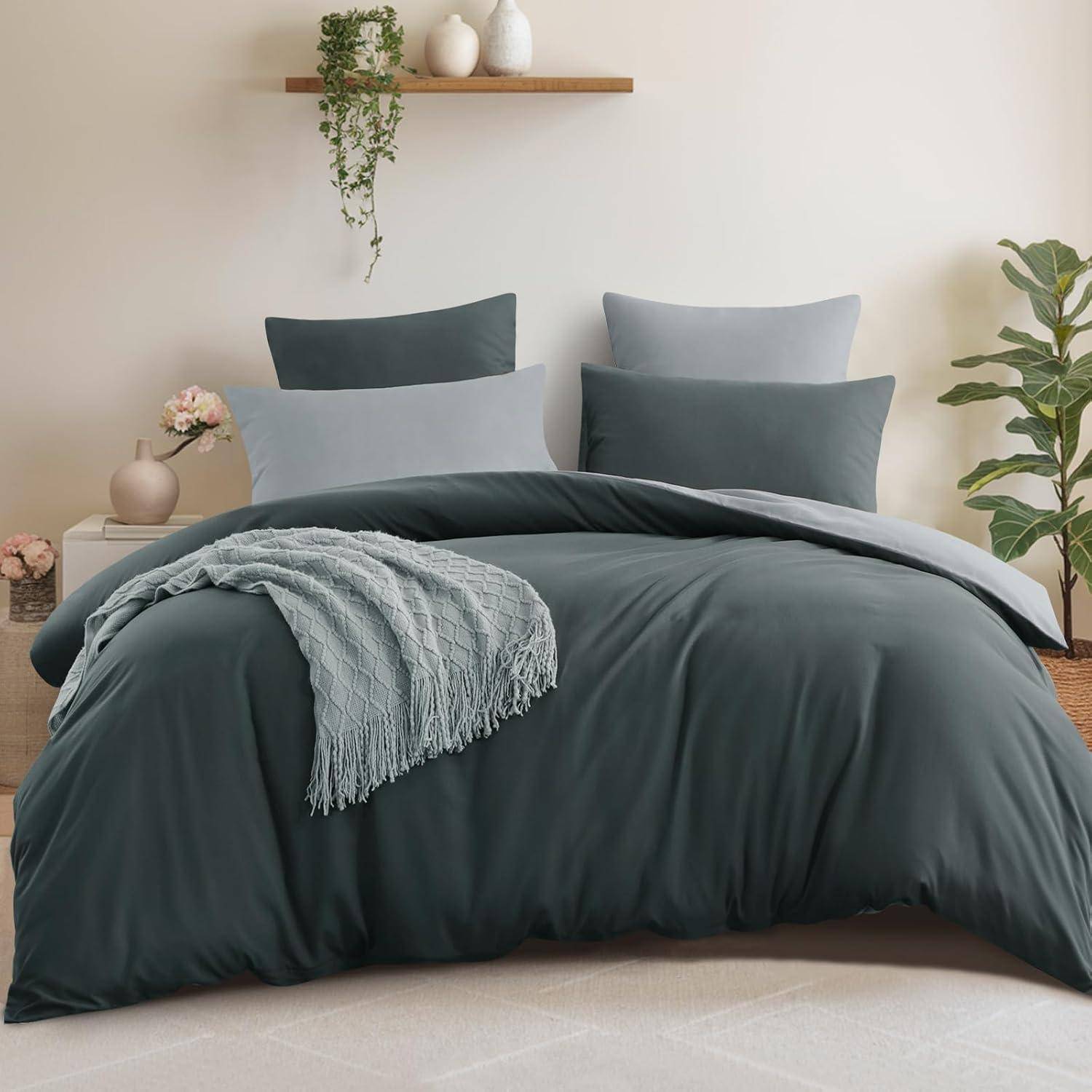 Ein ordentlich gemachtes Bett mit dunkelgrauer Bettwäsche, zwei grauen Kissen und einer zusammengelegten Decke. Pflanzen und Dekorationsgegenstände befinden sich auf einem Regal darüber.