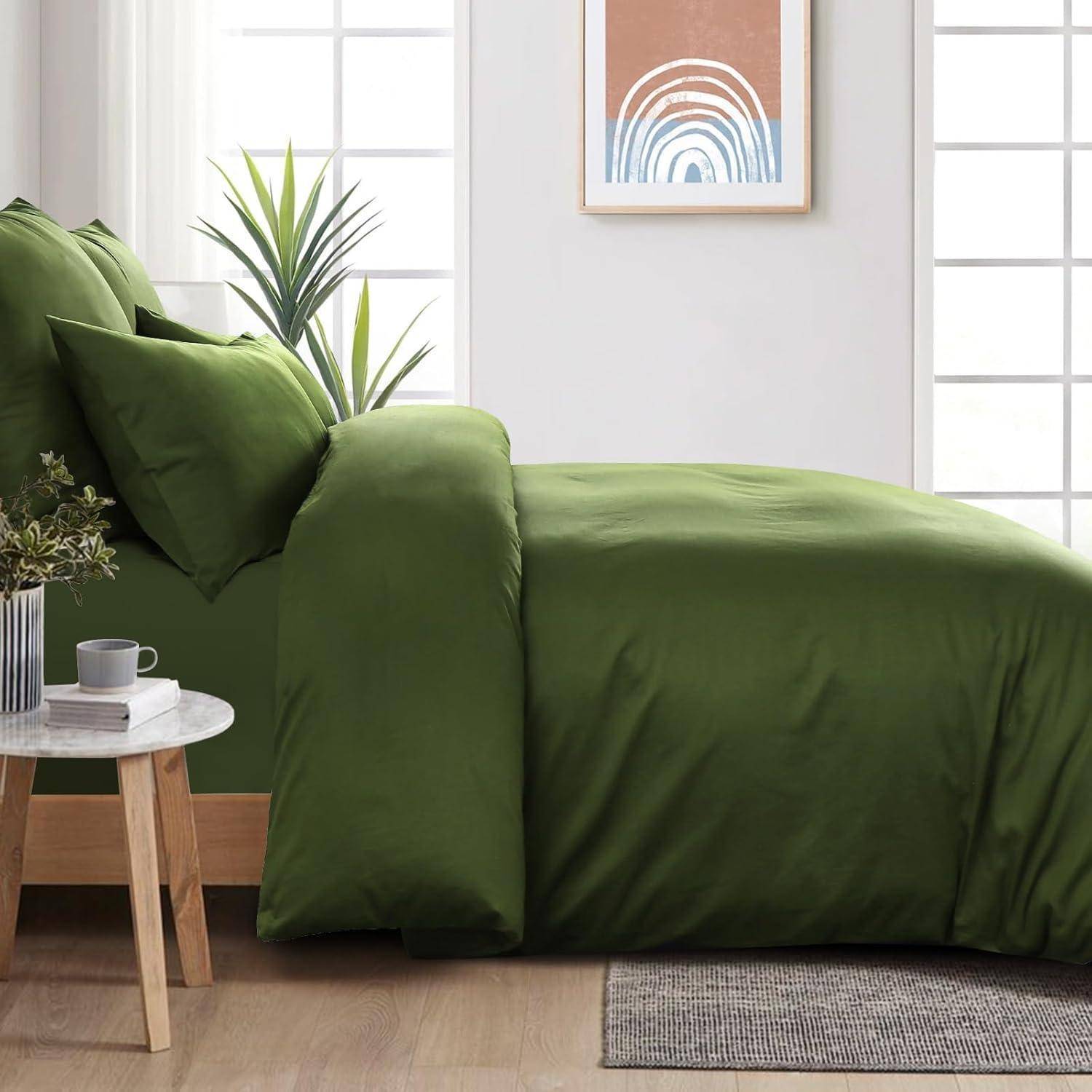 Ein Schlafzimmer mit einem ordentlich gemachten Bett, das mit grüner Bettwäsche bezogen ist, zwei dekorativen Pflanzen auf einer Holzbank und einem gerahmten abstrakten Kunstwerk an der Wand.