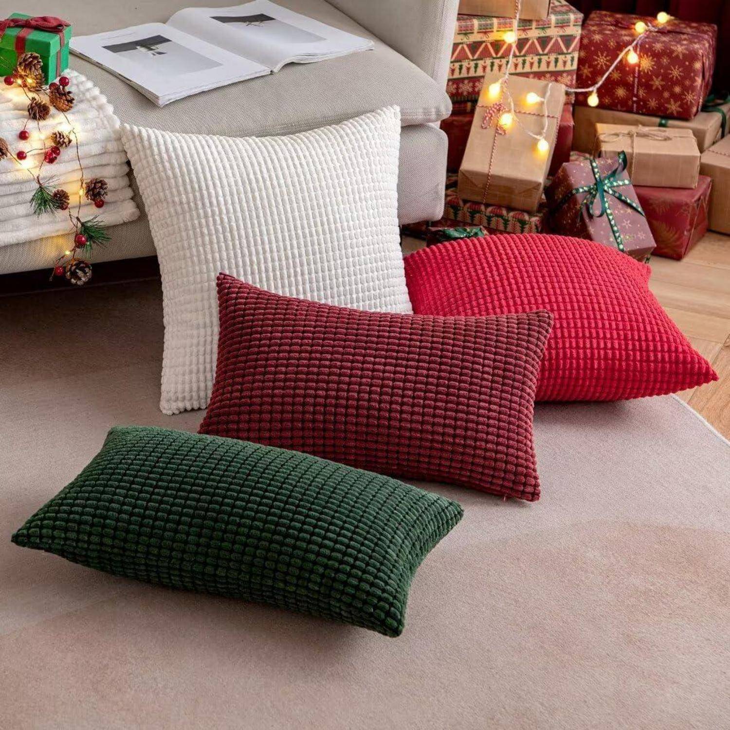 Festliche Wohnszene mit roten, grünen und weißen Kissen auf dem Boden, einem nahegelegenen Weihnachtsbaum mit Christbaumschmuck und eingepackten Geschenken.