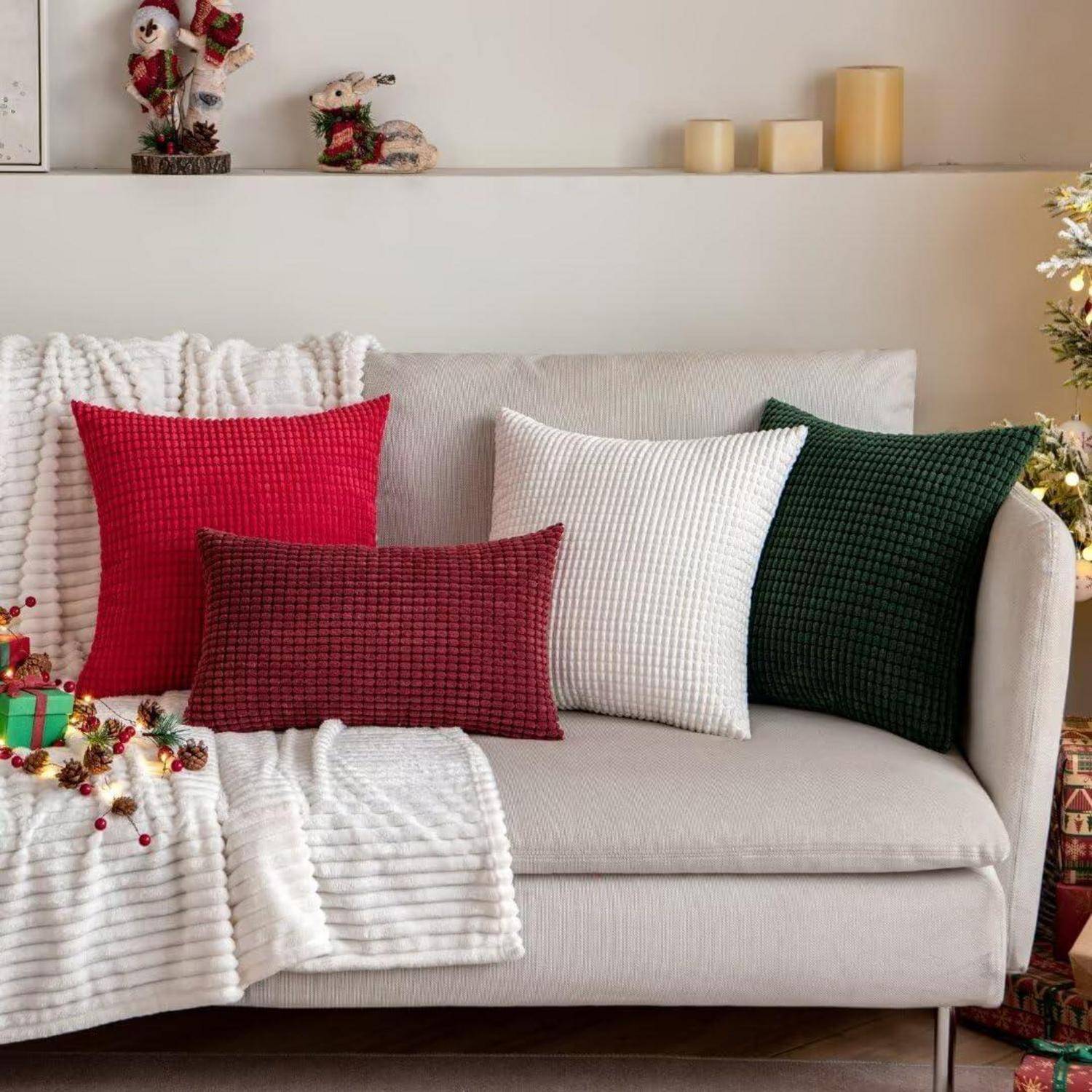 Ein gemütliches Wohnzimmer mit einem weißen Sofa, roten und grünen Weihnachtskissen und festlicher Dekoration, einschließlich Kerzen und einer kleinen Weihnachtsmannfigur.