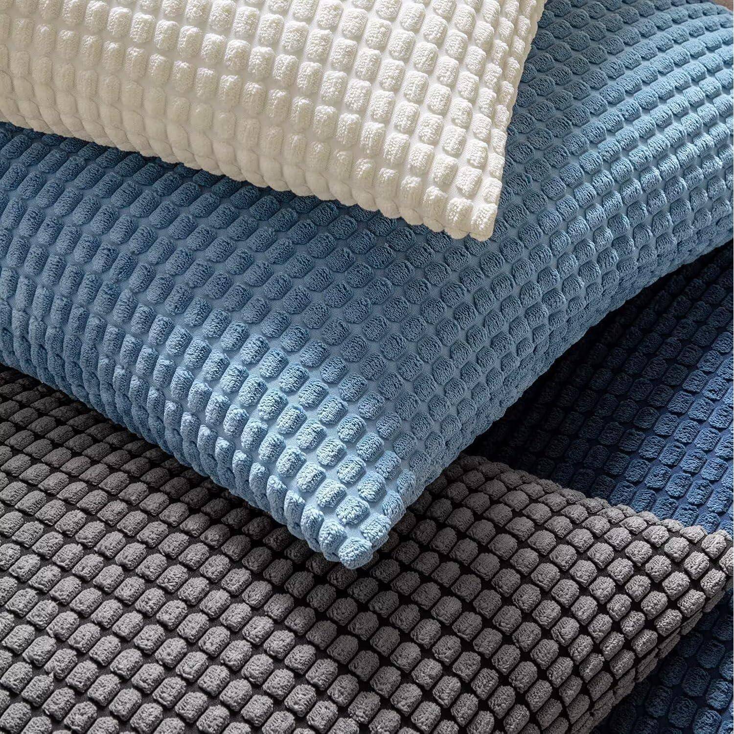 Ein Stapel von Kissen mit Strukturmuster in verschiedenen Farben: Weiß, Hellblau, Dunkelblau und Grau, die ein Waffelmuster aufweisen.