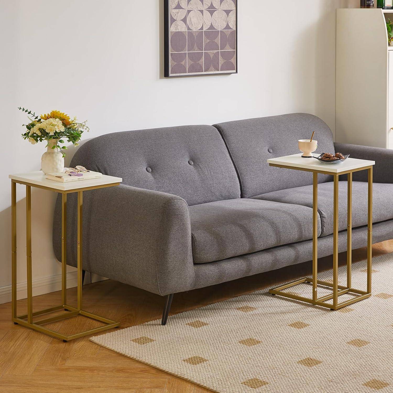 Ein moderner Wohnbereich mit einem grauen Sofa, sechseckiger Wandkunst, zwei Beistelltischen mit Pflanzen und Büchern sowie einem beigen Teppich auf Holzdielen.