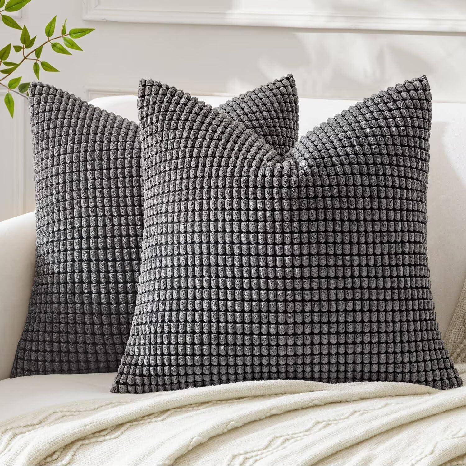 Zwei strukturierte graue Kissen liegen auf einem cremefarbenen Sofa mit einer weichen Decke, die über den Rand gehängt ist, und schaffen eine gemütliche und einladende Atmosphäre.