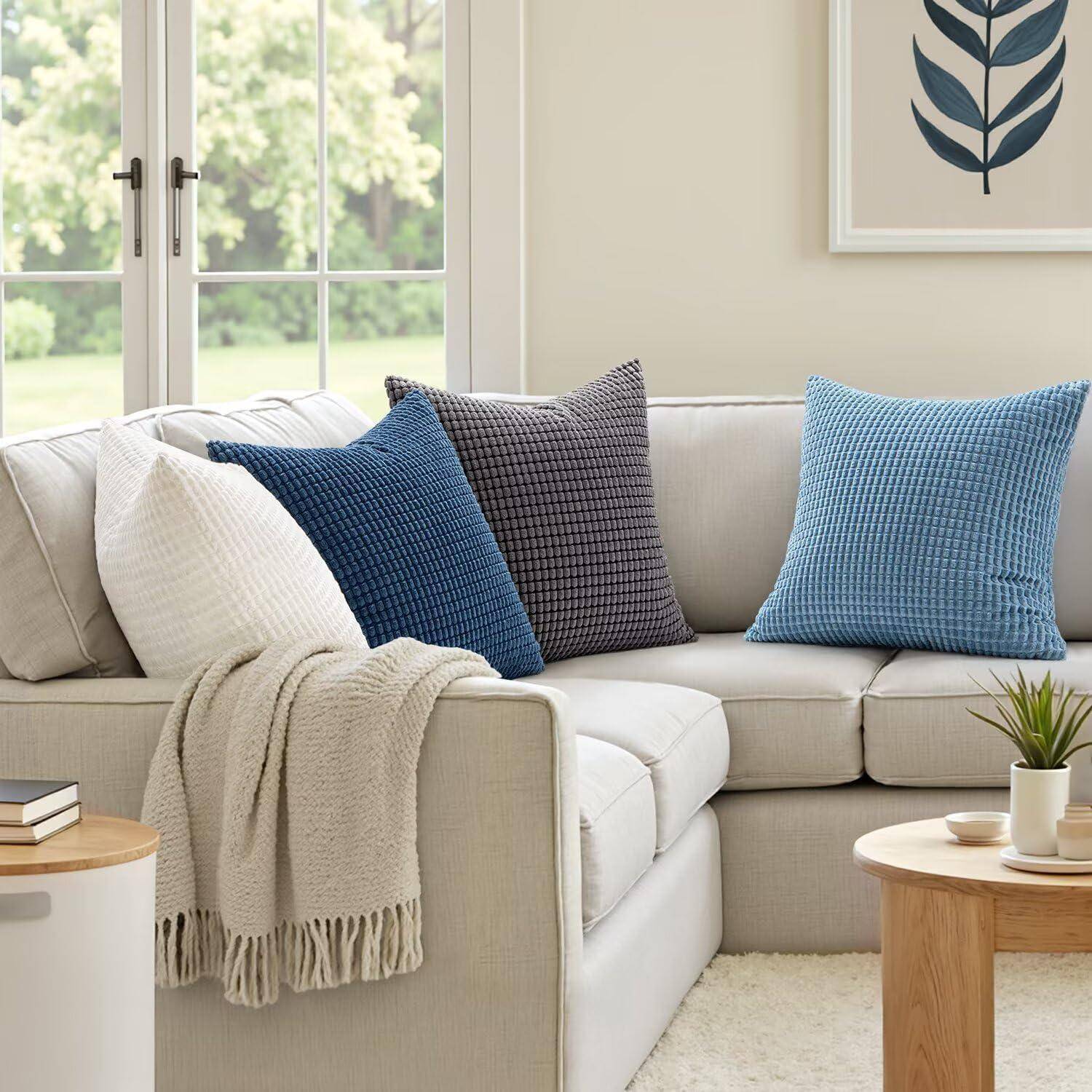 Ein gemütliches Wohnzimmer mit einem beigen Sofa, geschmückt mit weißen und blauen Kissen, einer Decke und einem kleinen Holztisch mit einer Pflanze.