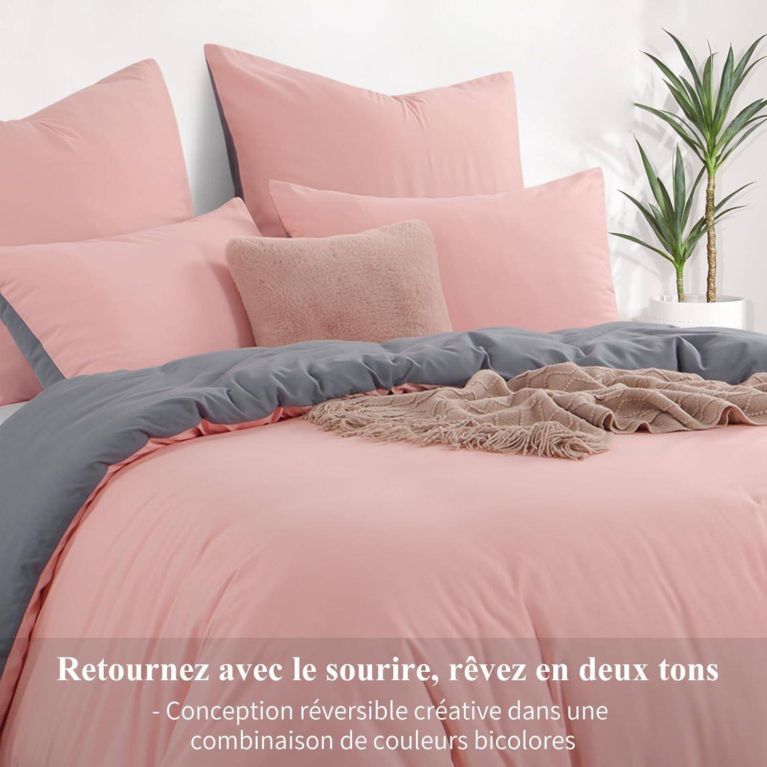 Rosa und grauer Bettwäsche-Set mit Kissen und Decke. Text auf Französisch lautet: ‚Kehren Sie mit einem Lächeln zurück, träumen Sie in zwei Tönen'.