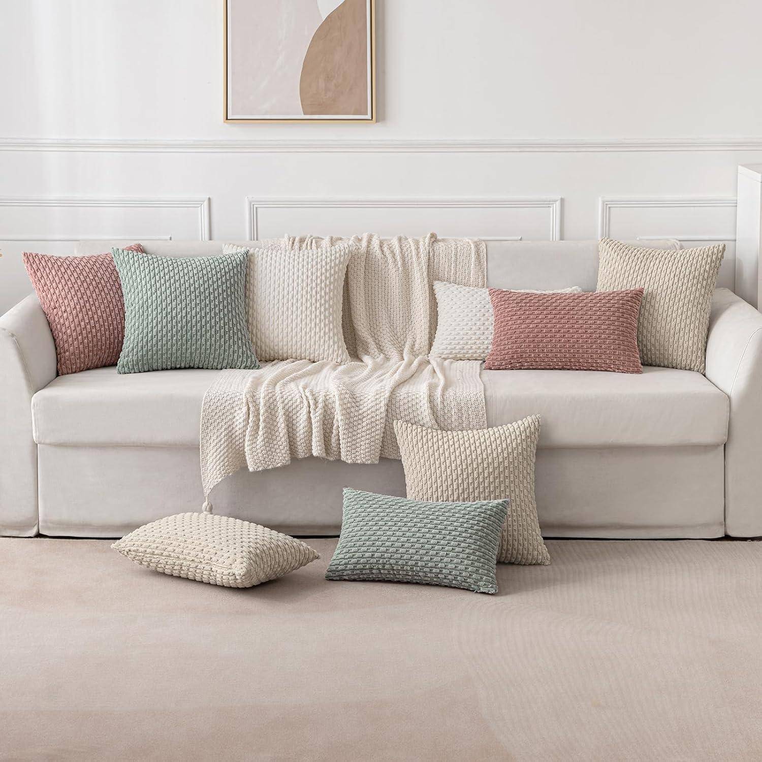 Ein weißes Sofa mit einer drappierten gestrickten Decke und pastellfarbenen Zierkissen in einem hellen Wohnzimmer mit einem minimalistischen gerahmten abstrakten Kunstwerk.