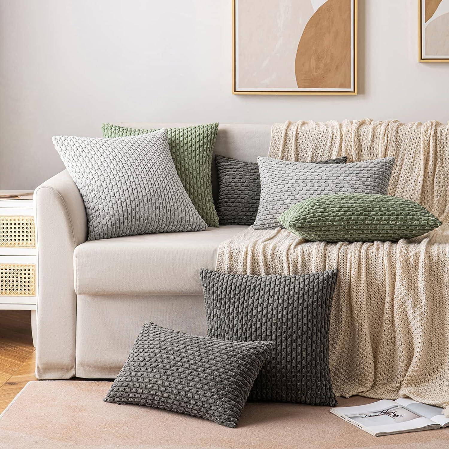 Ein gemütliches Wohnzimmer mit einem Sofa in neutralen Farbtönen, geschmückt mit strukturierten grauen und grünen Kissen. Abstrakte Kunstwerke hängen an der Wand darüber.