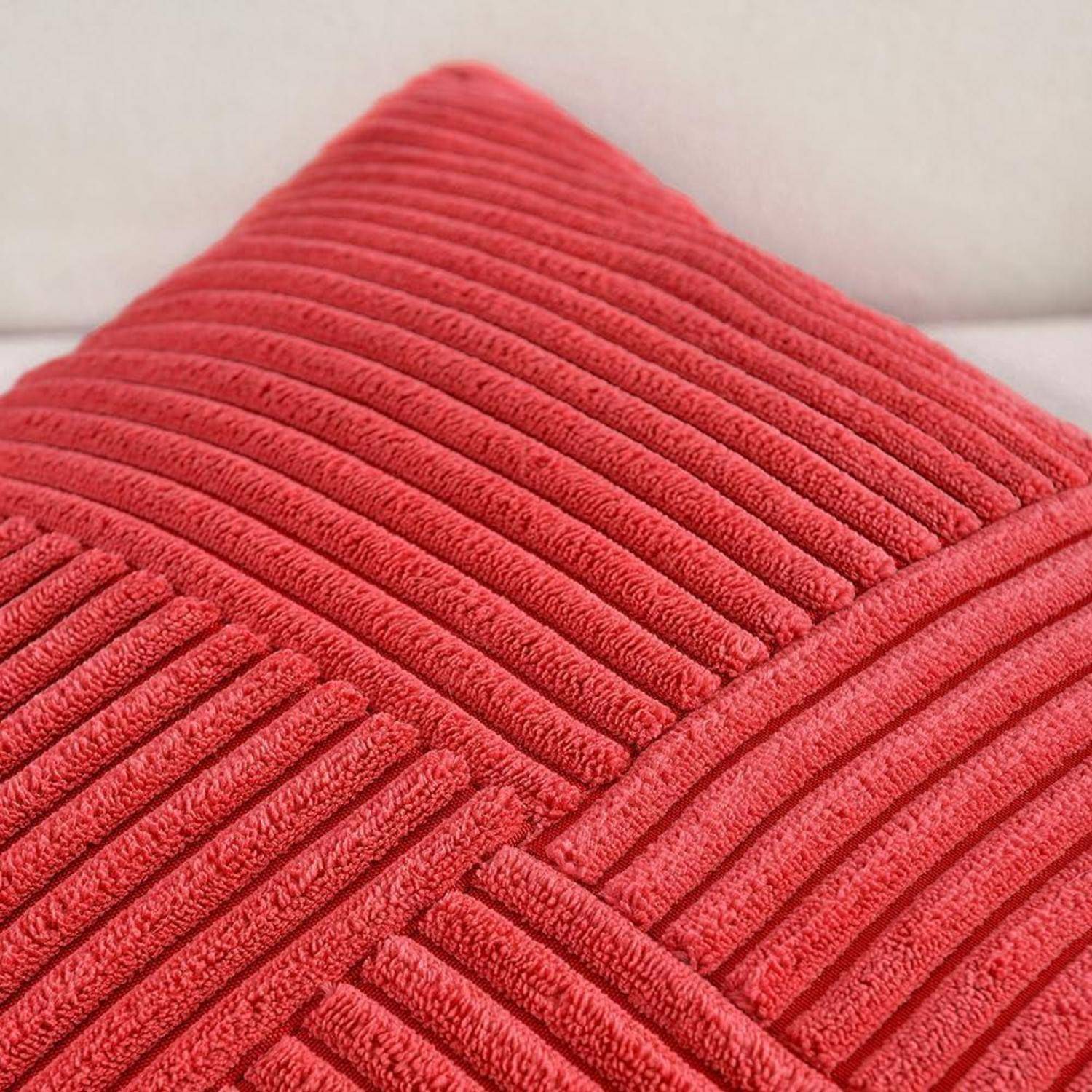 Rotes strukturiertes Kissen mit geripptem Muster auf einer weißen Oberfläche, das Details des Stoffes und den Farbenkontrast hervorhebt.