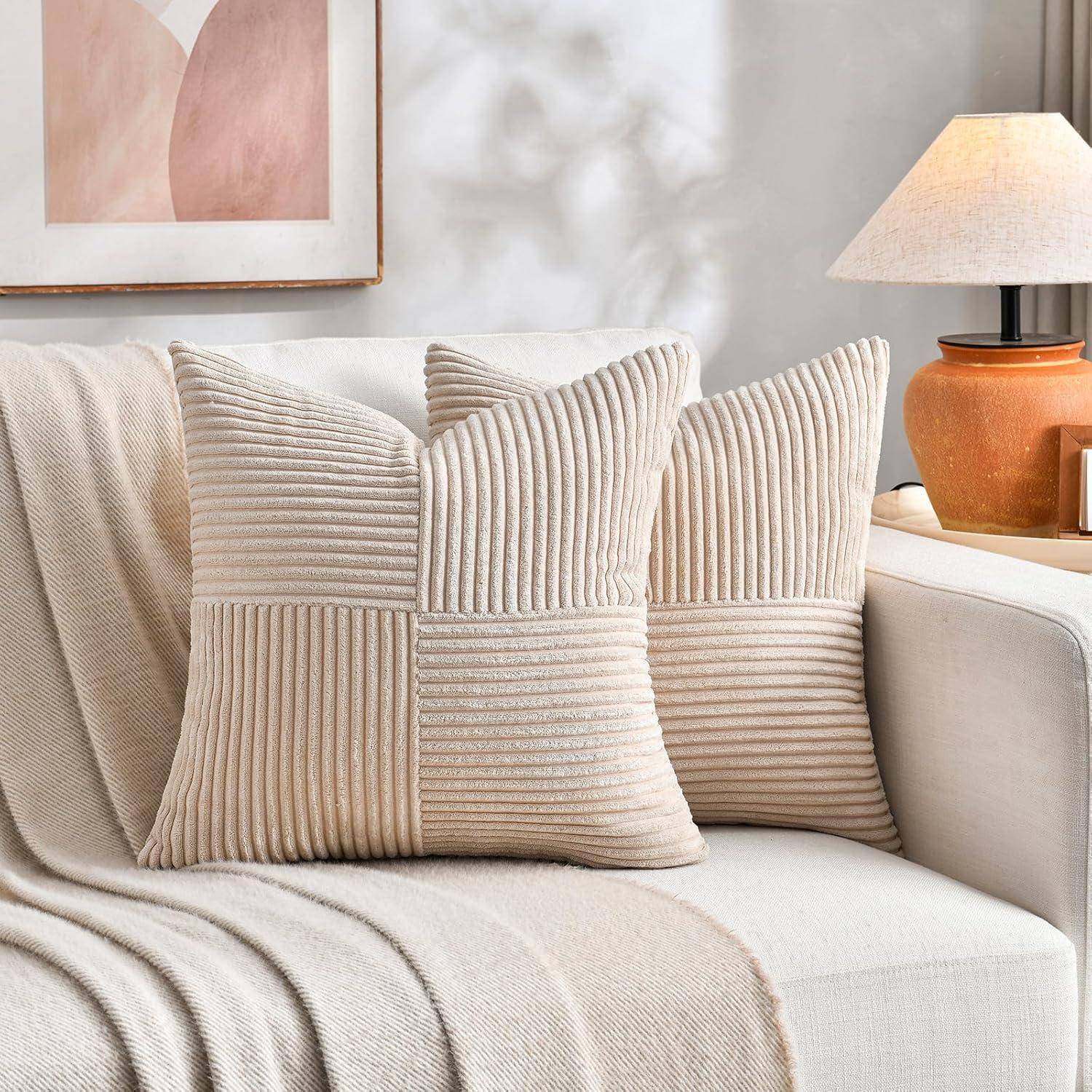 Ein gemütliches Wohnzimmer mit zwei gerippten beigen Kissen auf einem cremefarbenen Sofa. Eine weiche Decke bedeckt das Sofa, neben einer Lampe und einem gerahmten abstrakten Kunstwerk.