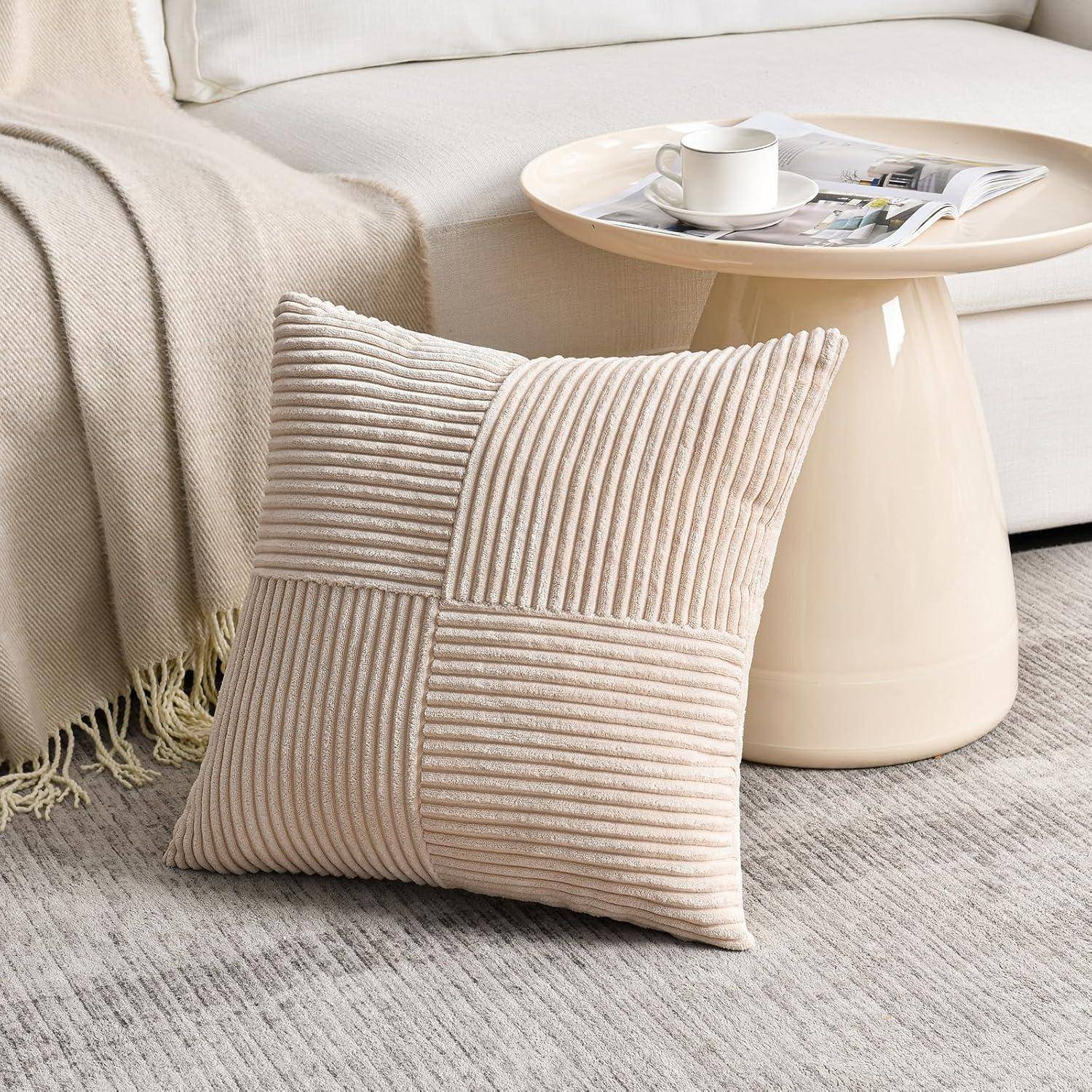 Ein beiger gerippter Kissen liegt auf einem grauen Teppich neben einem cremefarbenen Sofa und einem runden Beistelltisch, auf dem eine Kaffeetasse und eine Zeitschrift stehen.