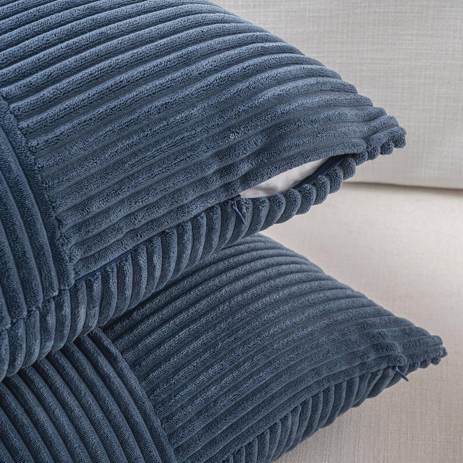 Zwei blaue Cordkissen, die übereinander auf einem hellgefärbten Sofa gestapelt sind und deren strukturierter Stoff eine gemütliche, einladende Atmosphäre vermittelt.