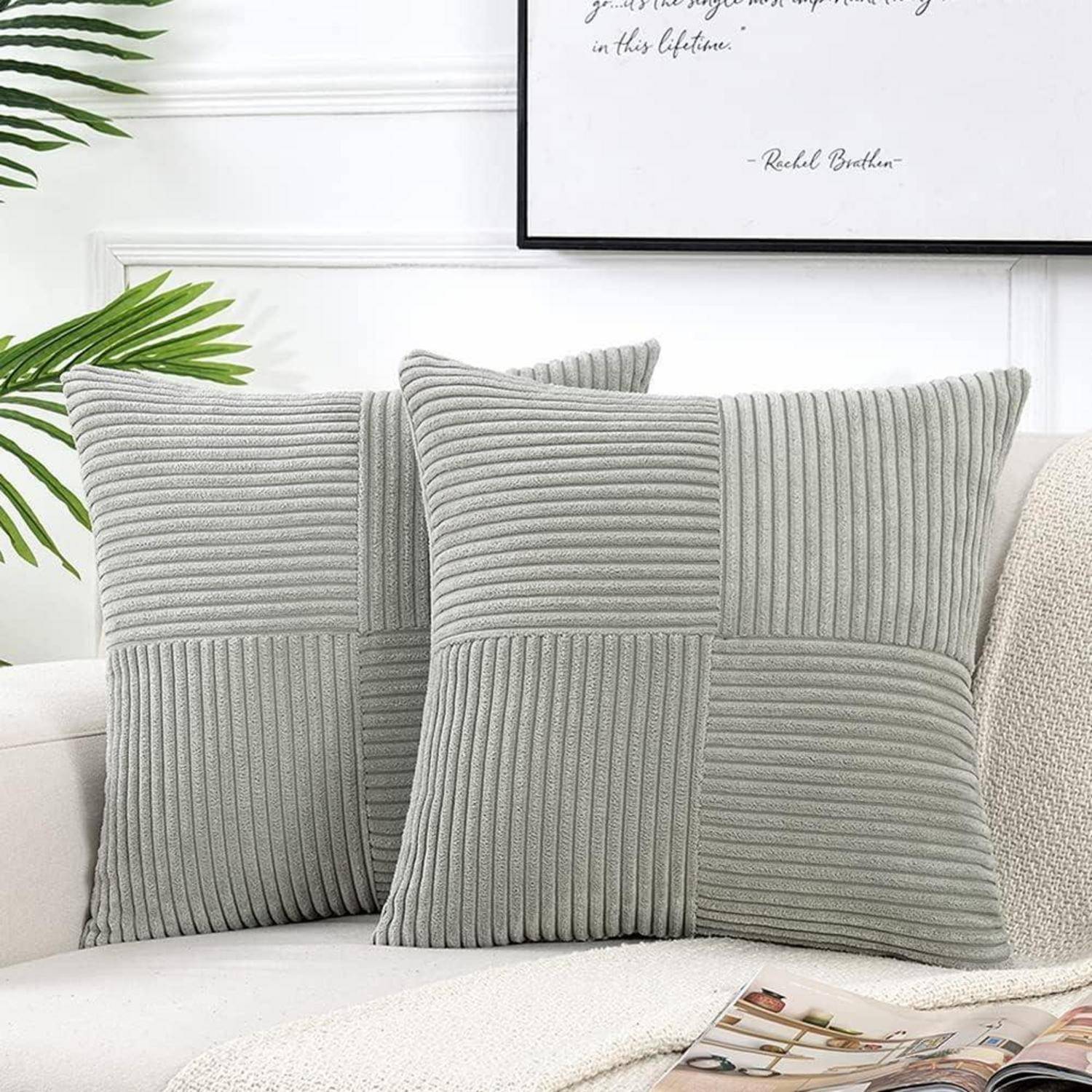 Zwei graue Cordkissen mit einem strukturierten Muster liegen auf einem weißen Sofa. Darüber hängt ein gerahmtes Zitat an der Wand.