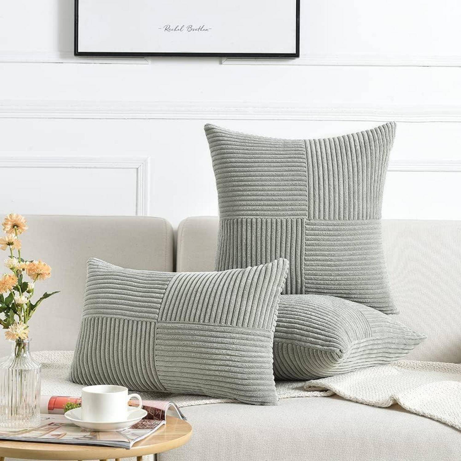 Eine gemütliche Wohnzimmer-Szenerie mit drei strukturierten grauen Kissen auf einem weißen Sofa, begleitet von einem Beistelltisch mit einer Tasse Kaffee und Blumen.