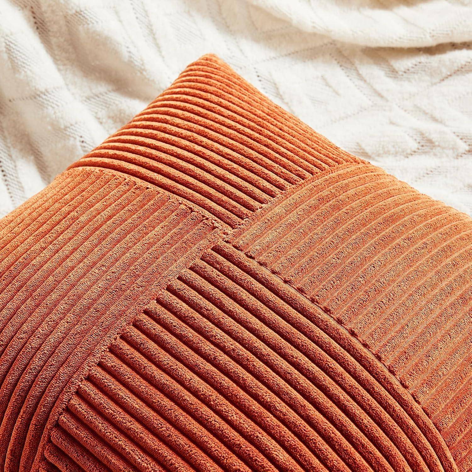 Nahaufnahme eines strukturierten orangefarbenen Kissens mit diagonalen Rillen, das auf einem weißen, gemusterten Stoffhintergrund liegt.