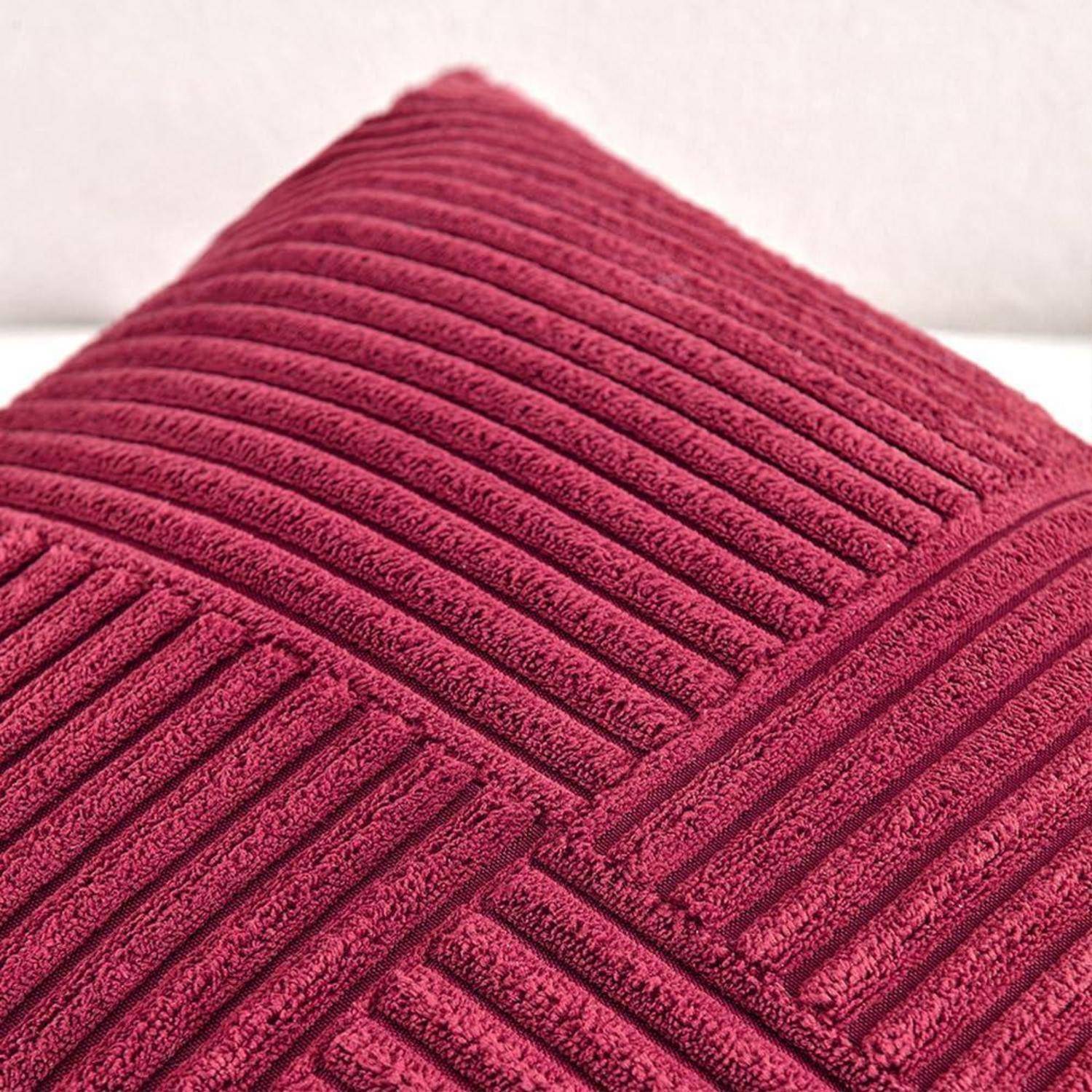 Ein strukturiertes, maroonefarbenes Kissen mit gestreiftem Muster wird vor einem blassen Hintergrund platziert.