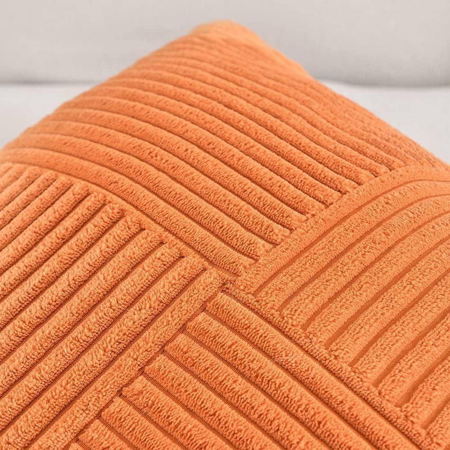 Ein orangefarbenes, geripptes Zierkissen auf einem hellgefärbten Sofa. Ideal, um Wärme und Stil zur Wohnzimmer- oder Schlafzimmereinrichtung hinzuzufügen.