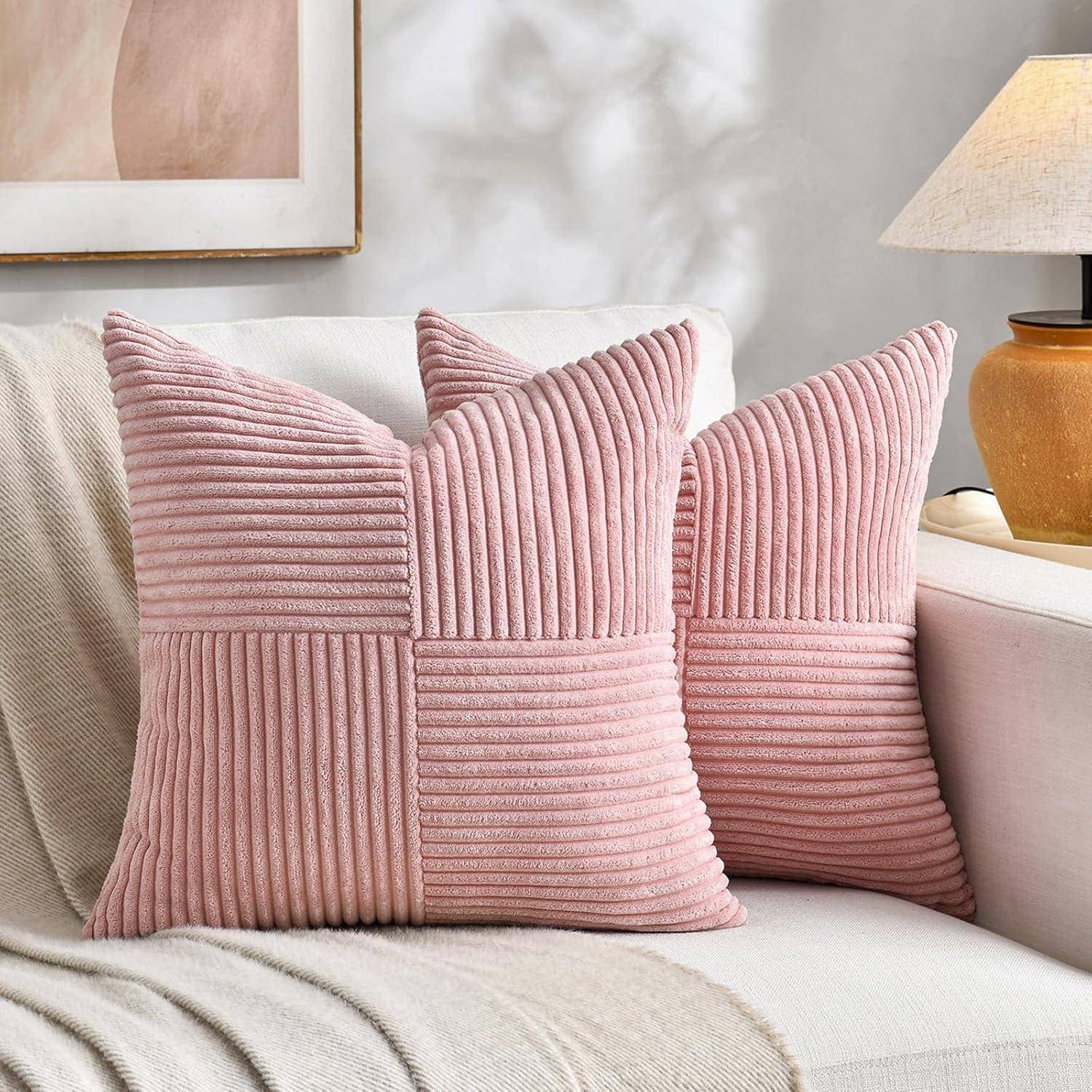 Zwei strukturierte rosa Kissen mit vertikalen und horizontalen Rillen liegen auf einem cremefarbenen Sofa in der Nähe einer warmbeleuchteten Lampe und schaffen eine gemütliche Atmosphäre.
