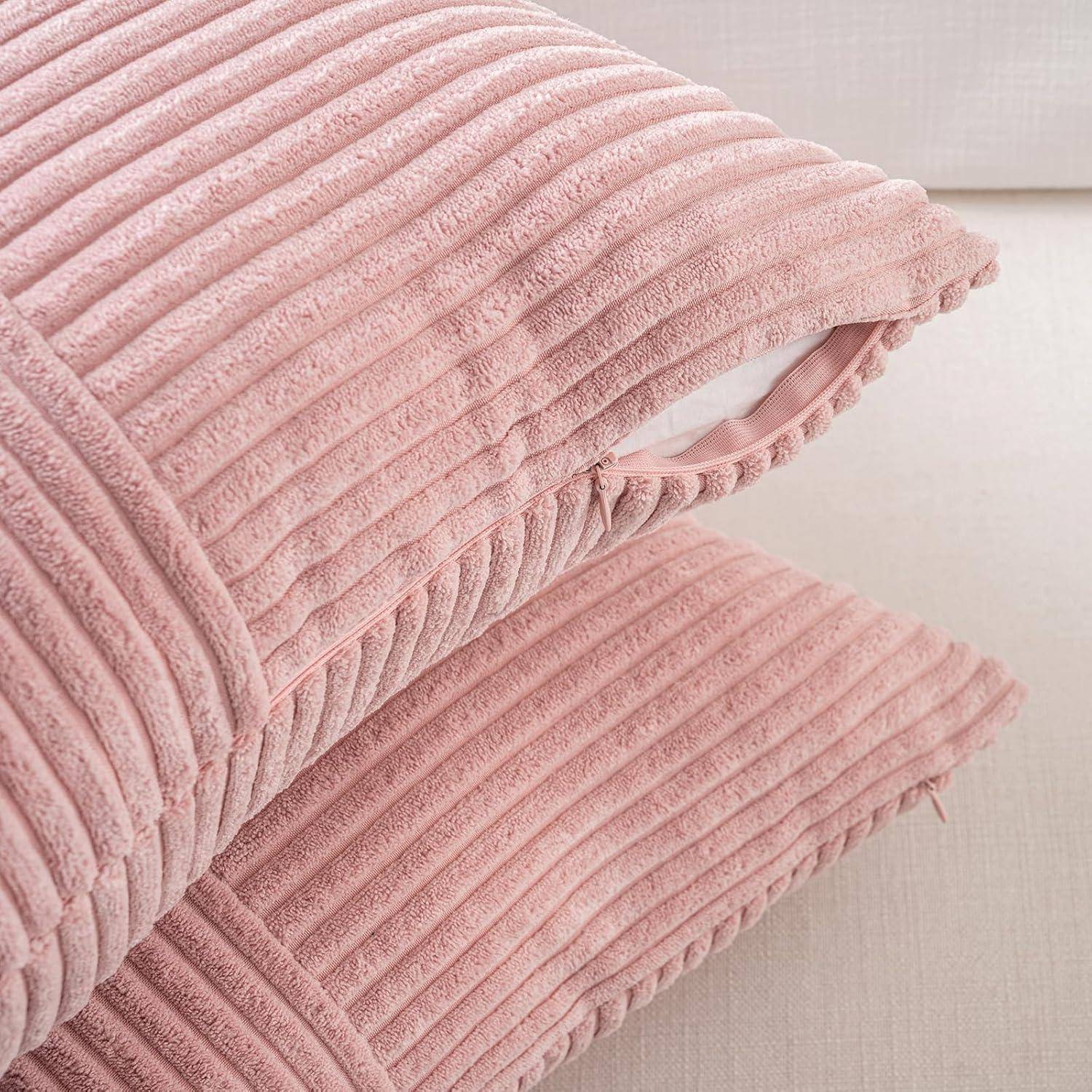 Ein Stapel von zwei rosa Cordkissen mit sichtbarer Strukturfabrik und weißem Innenfutter, auf einer helltonigen Oberfläche platziert.