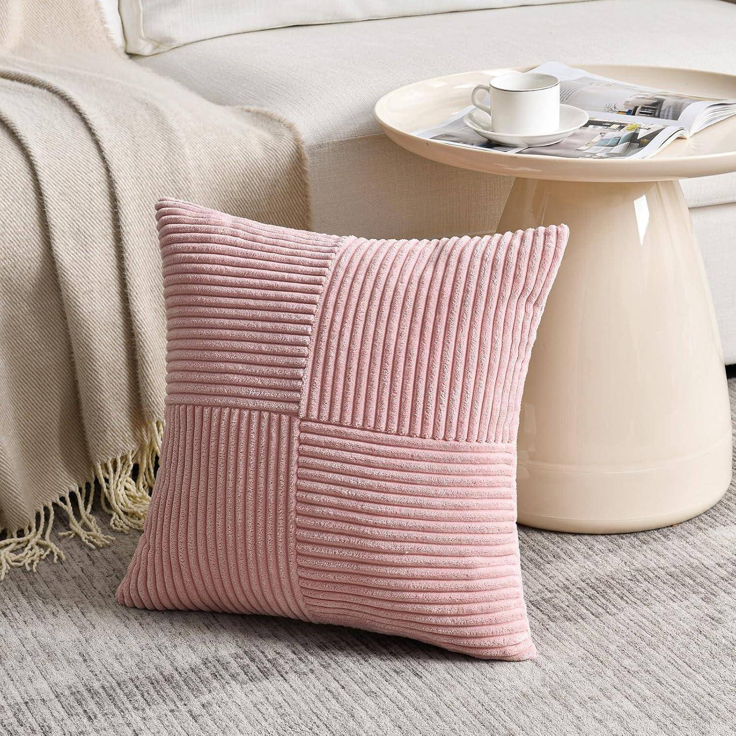 Ein rosa strukturiertes Kissen liegt auf einem grauen Teppich neben einem runden Couchtisch mit einer weißen Tasse und einer Zeitschrift, in der Nähe eines beigen Sofas mit einer Decke.