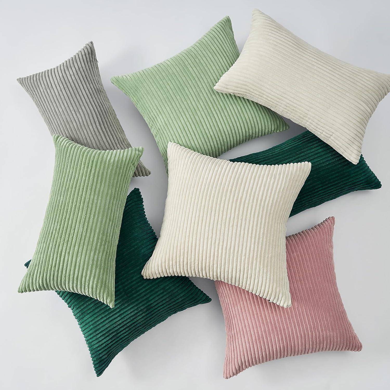 Mehrere gerippte Kissen in Grün-, Grau-, Beige- und Rosatönen sind überlappt auf einem schlichten Hintergrund angeordnet und präsentieren eine Vielfalt an Texturen.