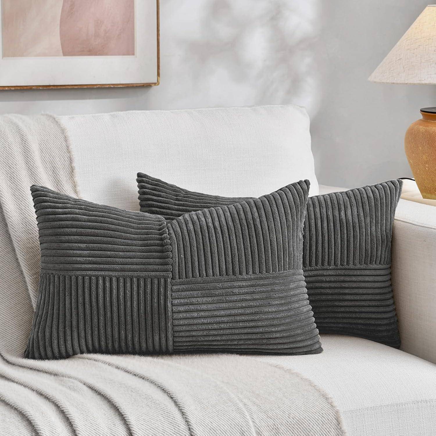 Ein beiger Sofa mit zwei strukturierten grauen Kissen. Ein gerahmtes abstraktes Kunstwerk hängt an der Wand, und eine Keramiklampe steht auf einem Beistelltisch.