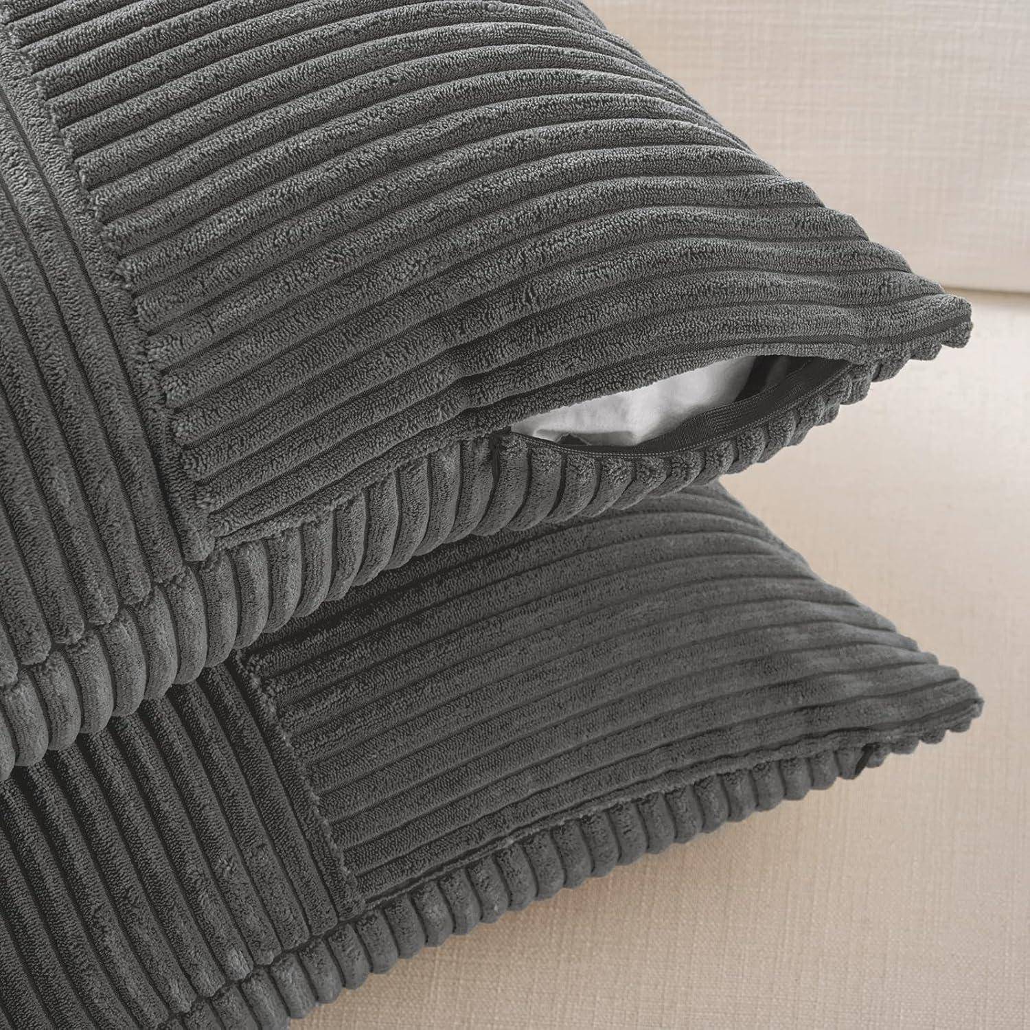 Zwei graue Cordkissen, übereinander gestapelt auf einem beigen Sofa, die ihre gerippte Textur und weichen Stofffasern hervorheben.