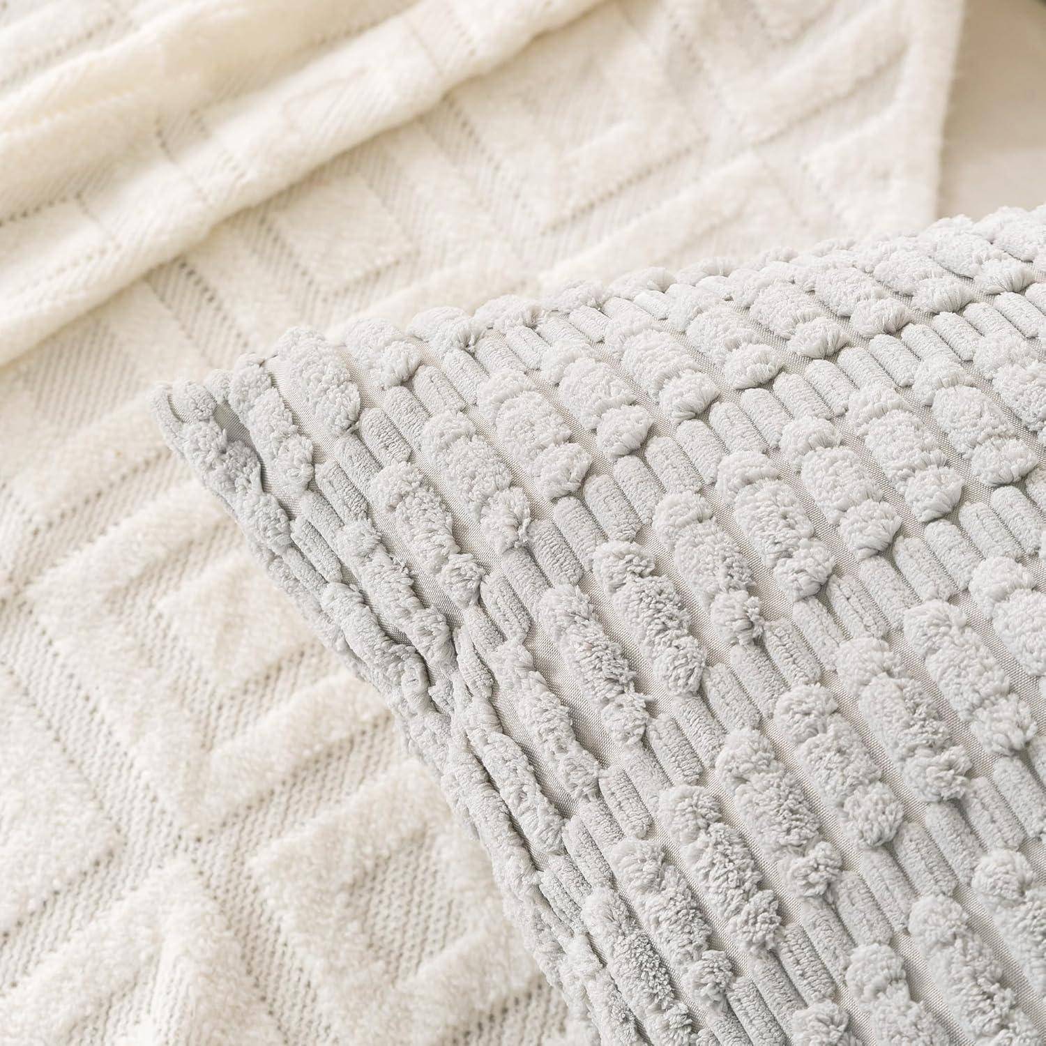 Ein strukturierter grauer Zierkissen auf einer cremefarbenen Strickdecke, der eine gemütliche und einladende Atmosphäre ausstrahlt.