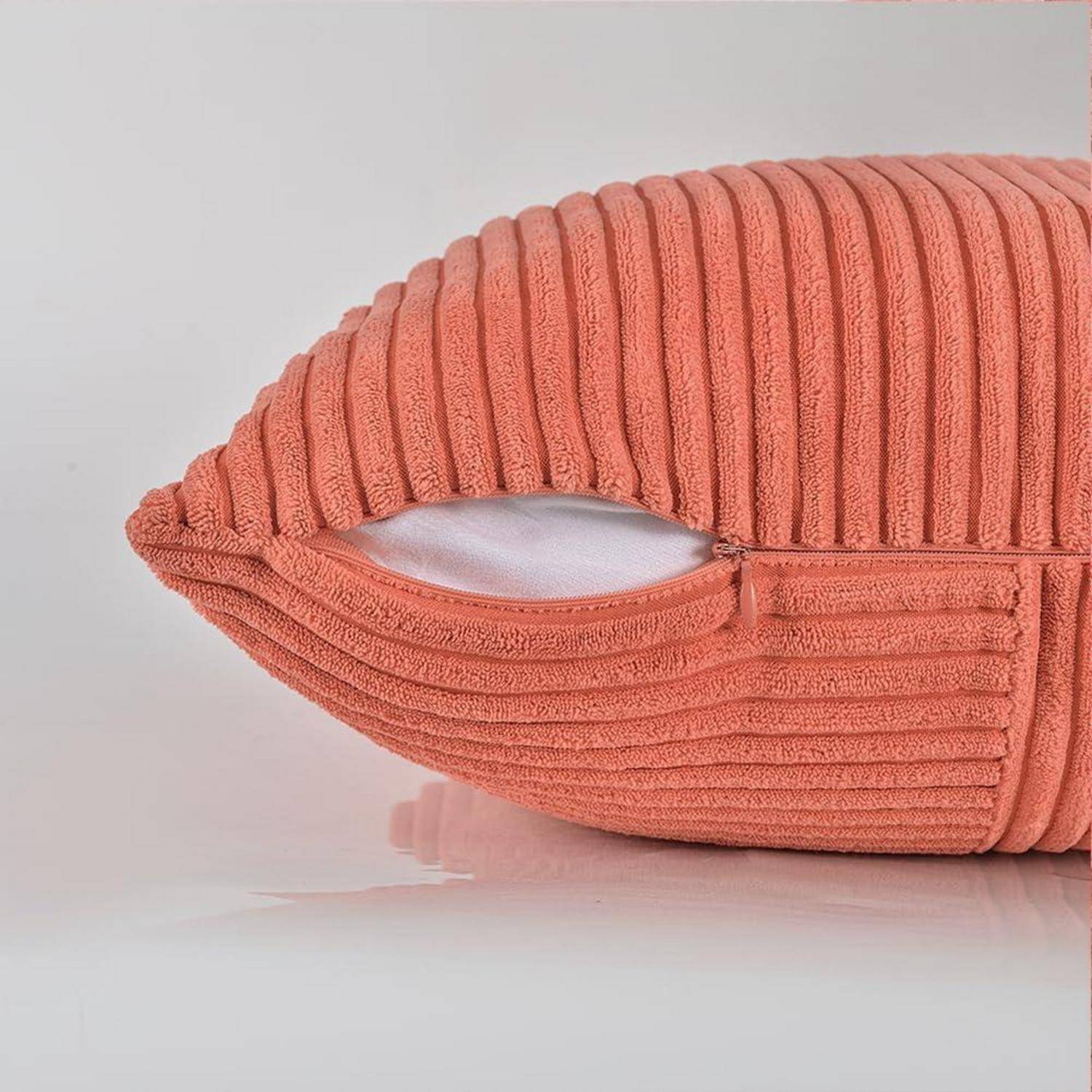 Ein rosa geripptes Kissen mit weicher Textur ruht auf einer reflektierenden Oberfläche. Seine Hülle ist leicht geöffnet und gibt eine weiße Innenfütterung frei.