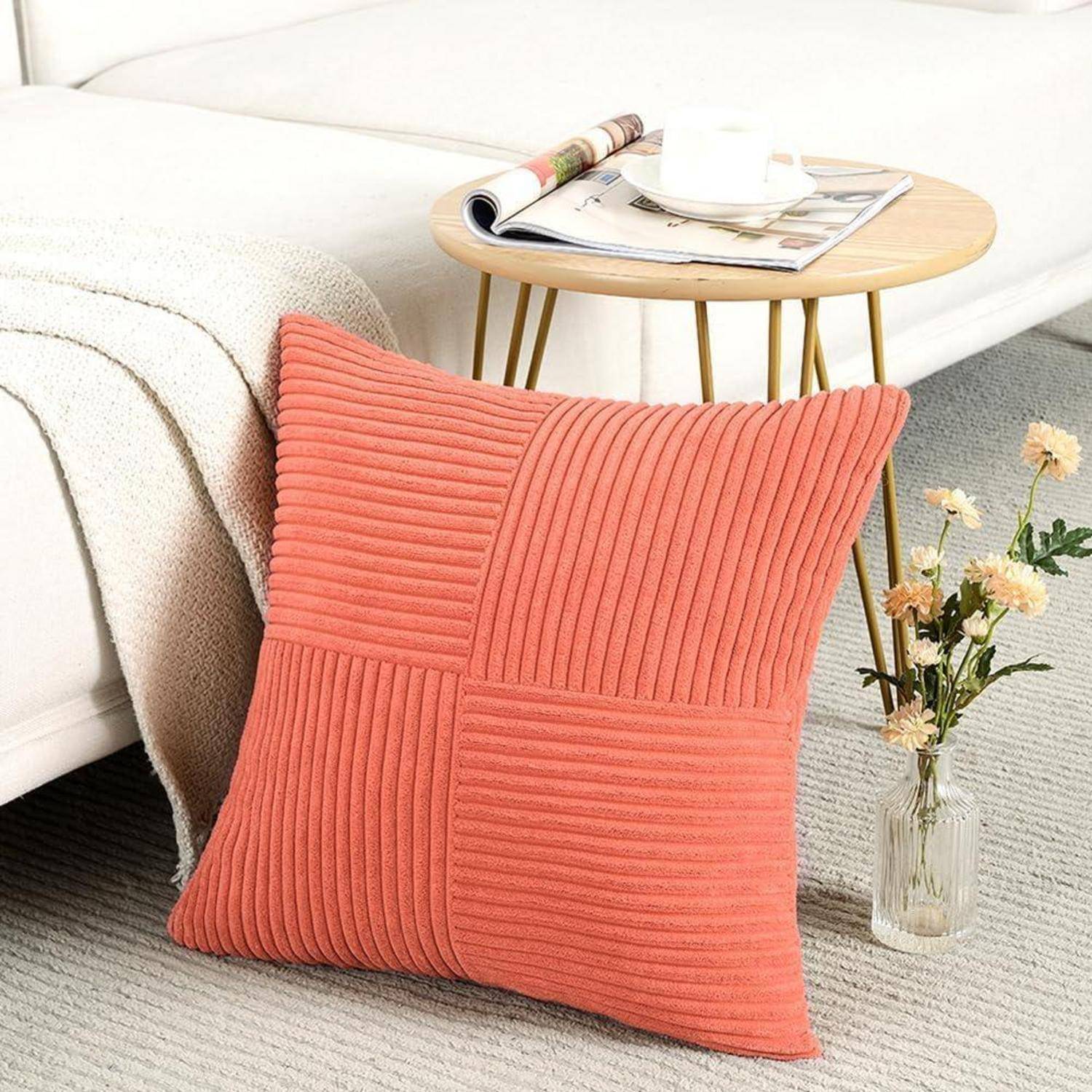 Ein strukturiertes Korallenkissen lehnt an einem cremefarbenen Sofa, während im Hintergrund ein kleiner runder Tisch eine Zeitschrift und eine Blumenvase trägt.