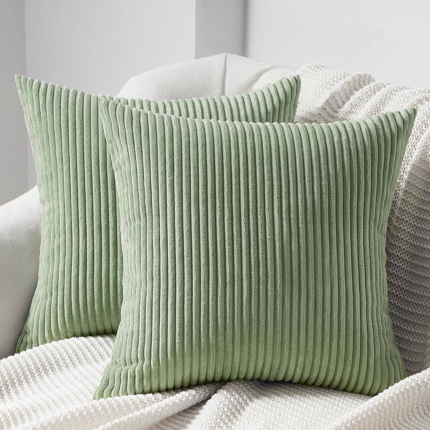 Zwei grüne gerippte Kissen auf einem cremefarbenen Sofa mit einer texturierten weißen Decke. Eine gemütliche und einladende Wohnzimmereinrichtung.