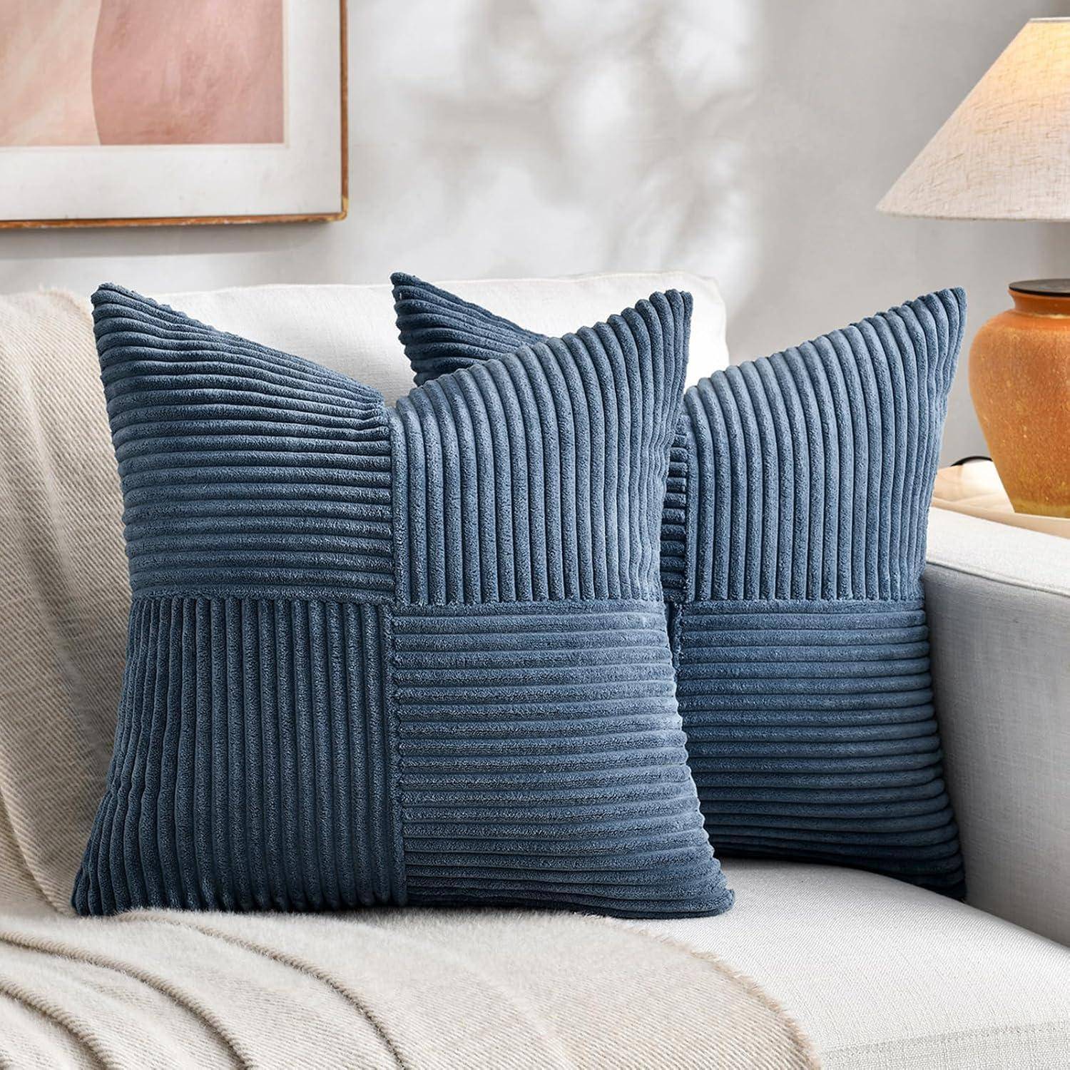 Zwei blaue Cordkissens mit vertikalen und horizontalen Streifen auf einem beigen Sofa, neben einer Lampe und abstrakter Wandkunst.