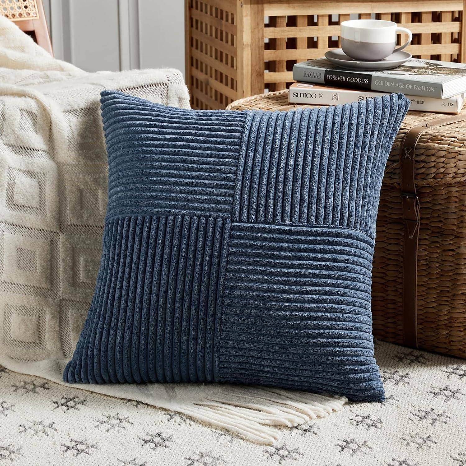 Ein blauer Cordkissen auf einem beigen Sofa neben einem geflochtenen Korb, der Bücher und eine weiße Tasse enthält, schafft eine gemütliche Wohnzimmeratmosphäre.