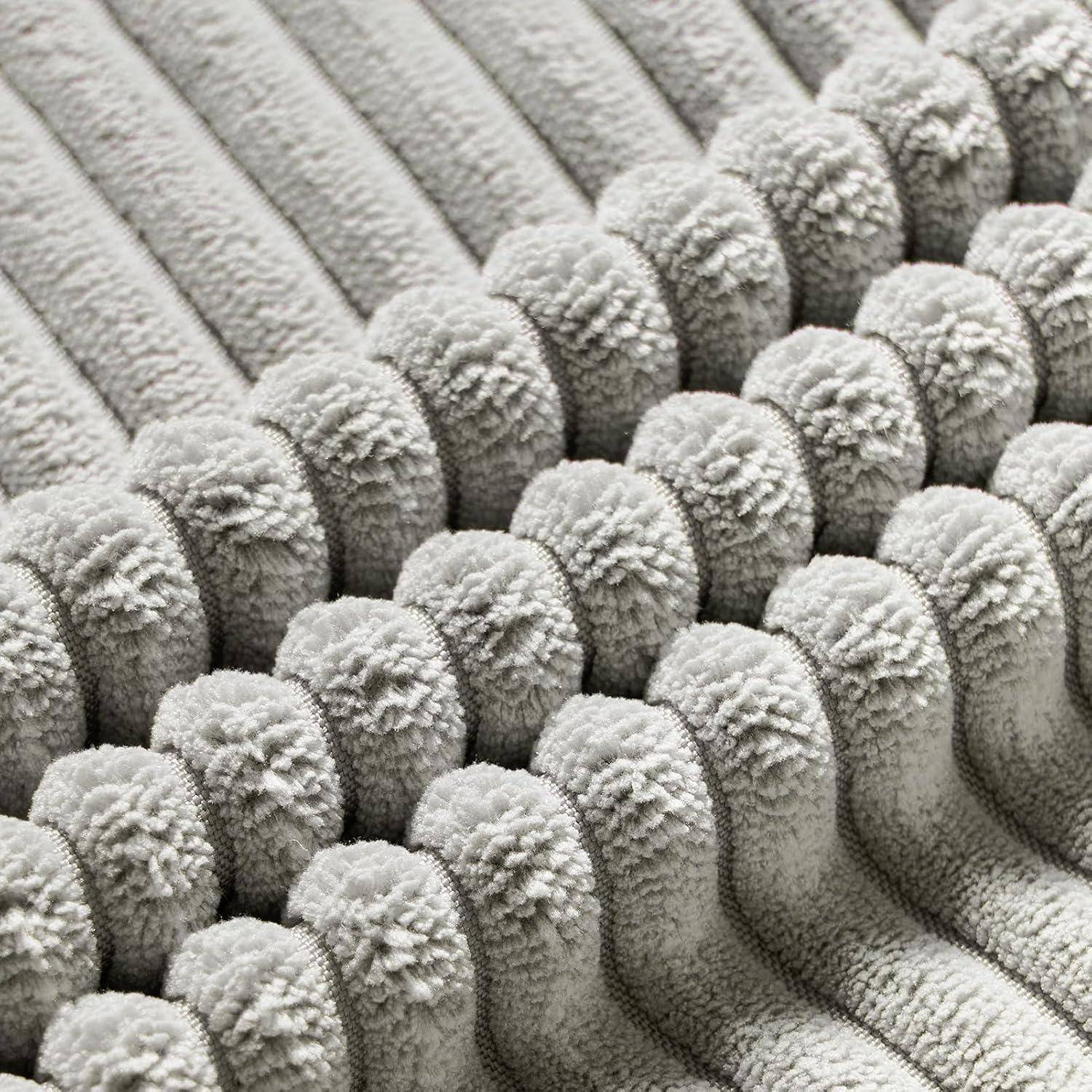 Nahaufnahme eines plüschigen, strukturierten grauen Stoffes mit sich wiederholenden abgerundeten Rillen, die einen weichen und gemütlichen Eindruck vermitteln.