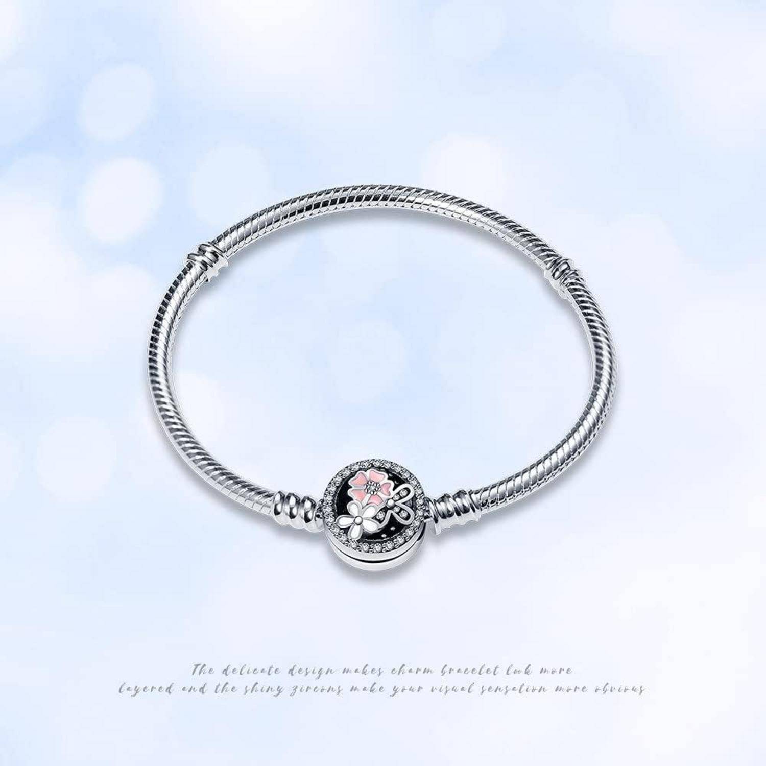 Ein silbernes Bettelarmband mit einem zentralen Blumenanhänger, der rosa und weiße Akzente auf einem hellblauen, unscharfen Hintergrund trägt.