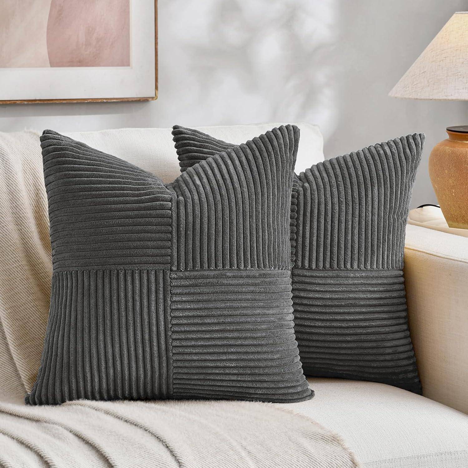 Zwei graue, strukturierte Kissen mit Quadratmuster sitzen auf einem cremefarbenen Sofa in einem hell erleuchteten Wohnzimmer.