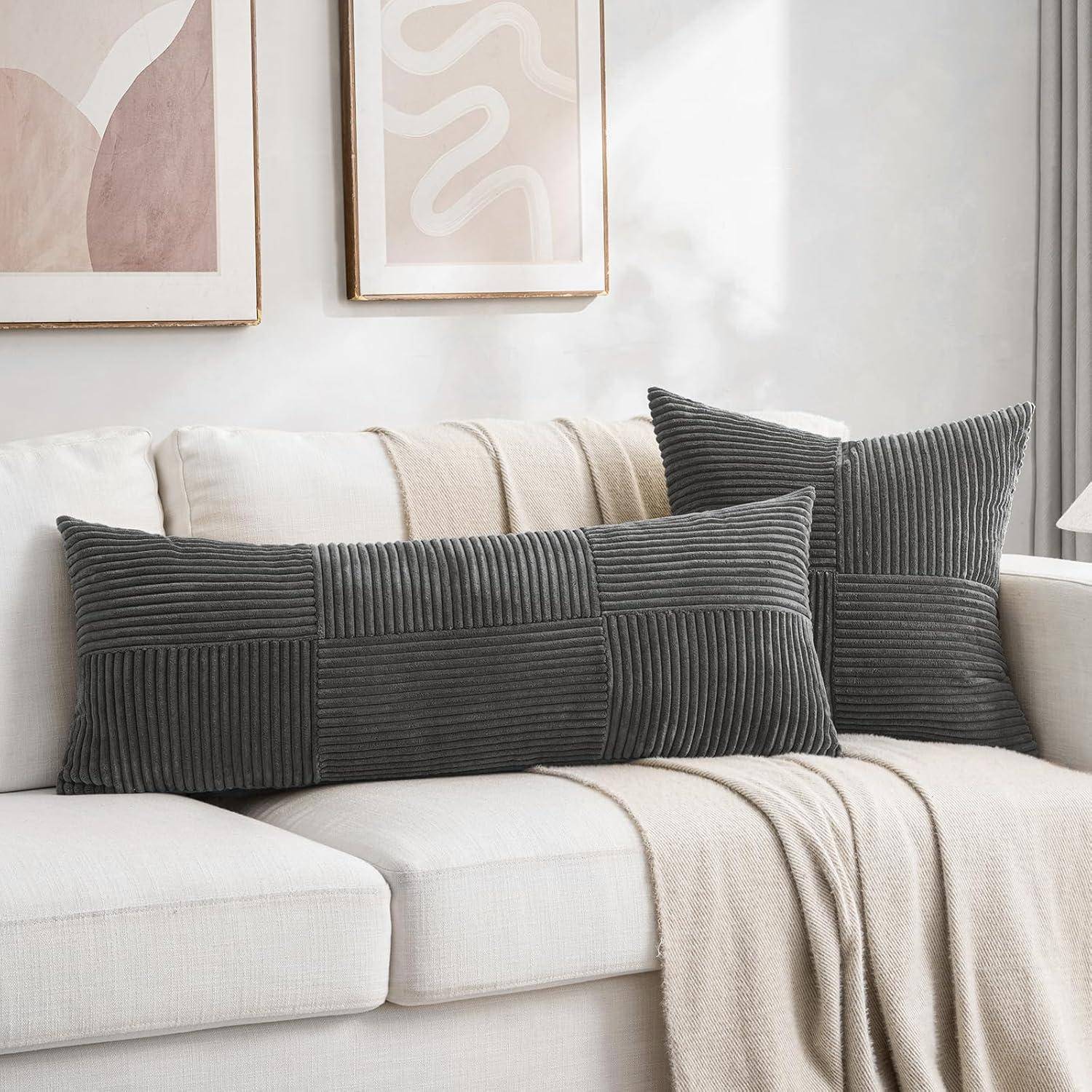Ein weißes Sofa mit einem beigen Überwurf und dunkelgrauen strukturierten Kissen, vor einer Wand mit abstrakten Kunstwerken in weichen, neutralen Tönen.