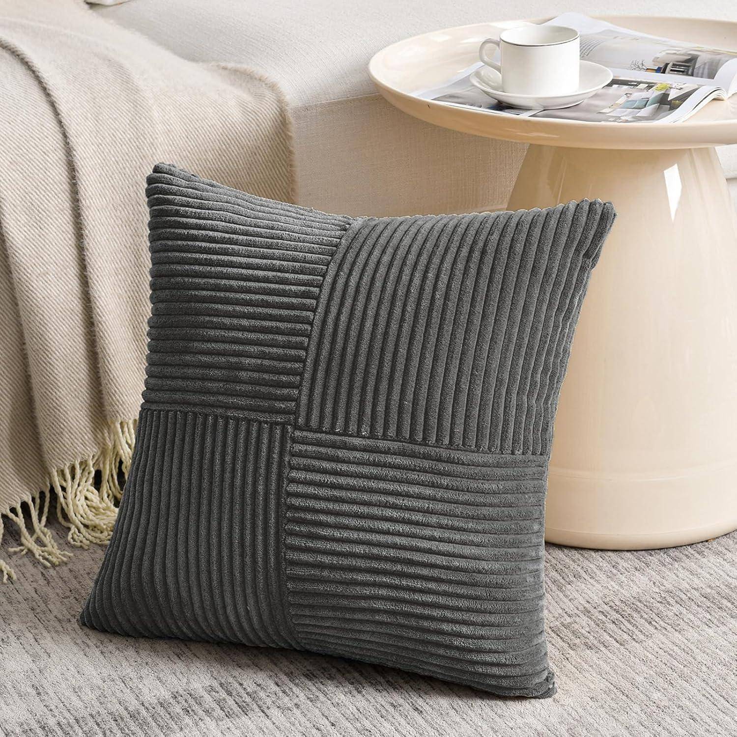 Ein grauer, kordähnlich strukturierter Zierkissen lehnt an einer beigen Couch mit Quastendetail, neben einem kleinen, runden weißen Tisch mit einer Kaffeetasse.