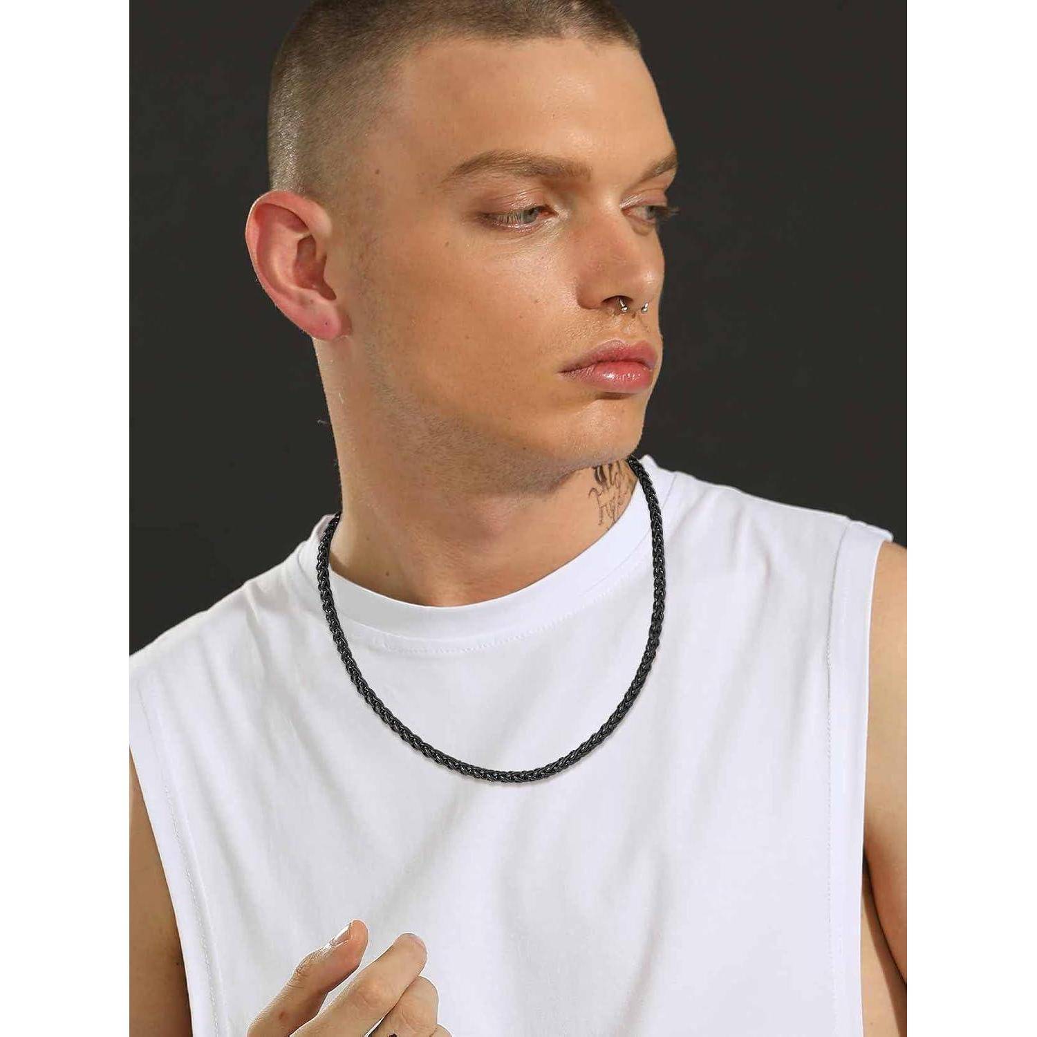 Mann in einem weißen ärmellosen Shirt und einer schwarzen Halskette, seitlich blickend vor einem dunklen Hintergrund.