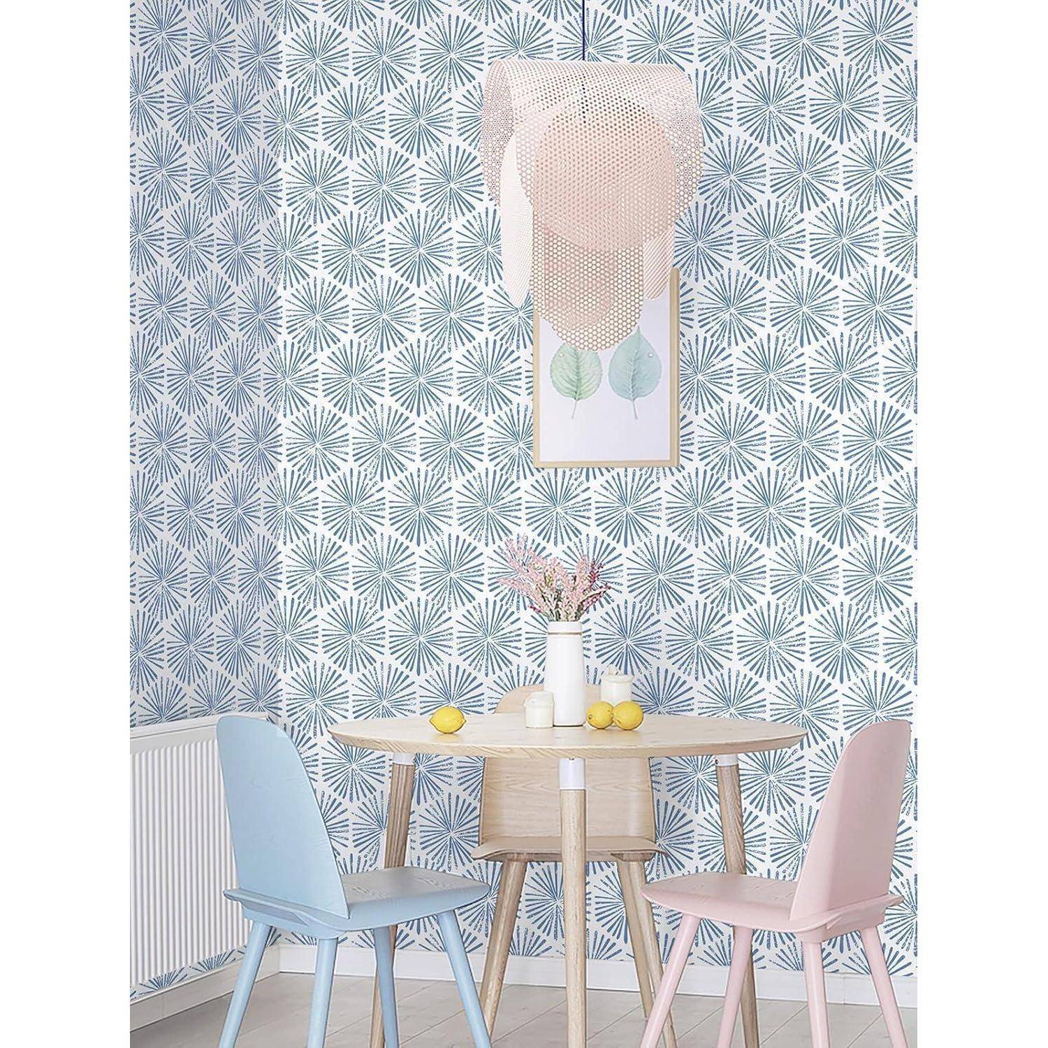 Ein pastellfarbener Essbereich mit einem runden Holztisch, zwei Stühlen (einer blau, einer rosa), einer kleinen Vase mit Blumen, vier Zitronen und gemusterter Tapete.