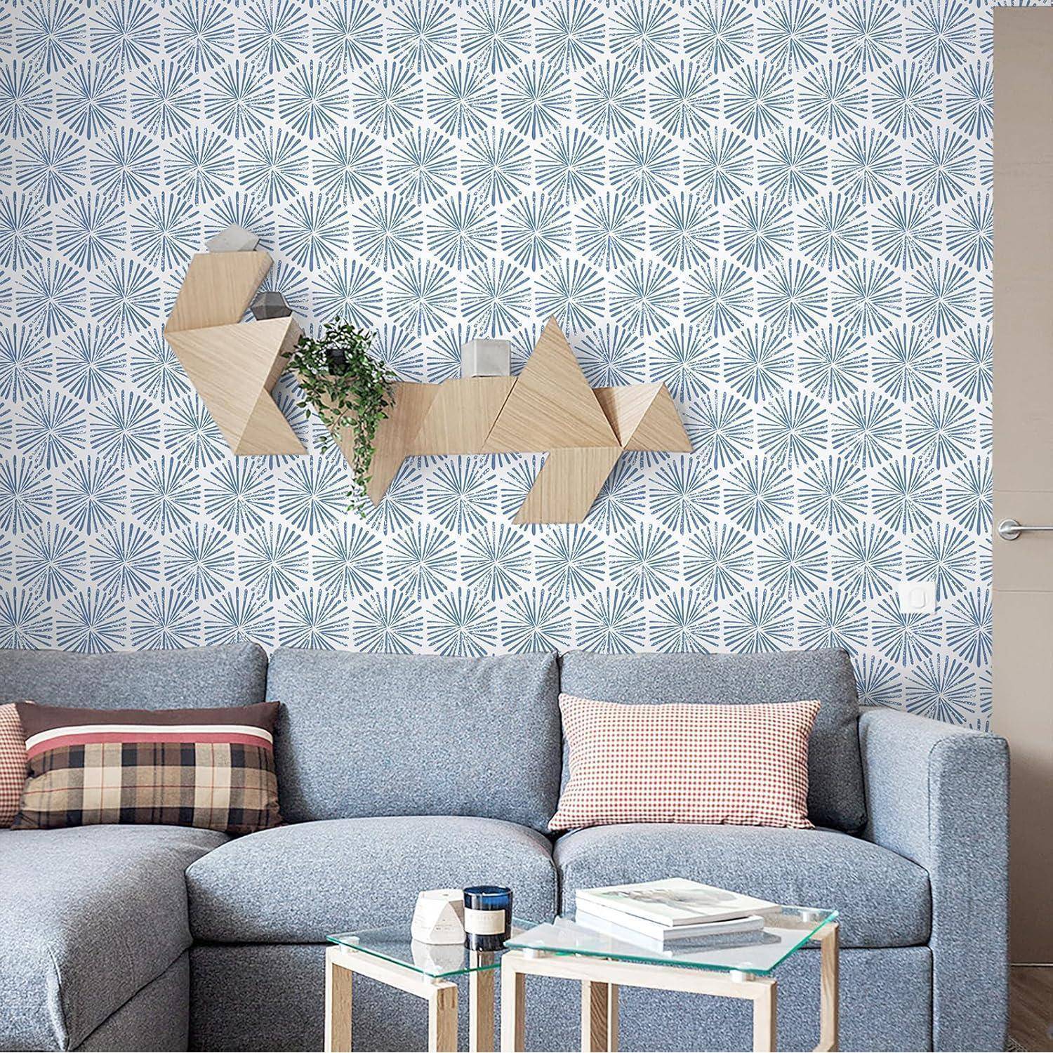 Ein modernes Wohnzimmer mit einem blauen Sofa, geometrischer Wandkunst und einer gemusterten Tapete. Die Tischplatte ist mit Büchern und Dekorationsgegenständen bestückt.